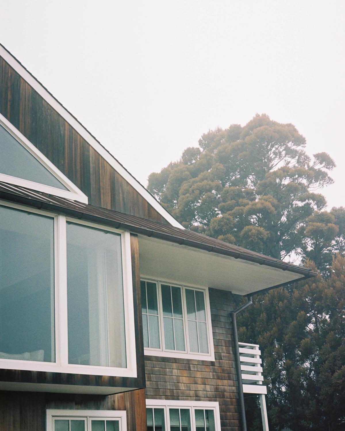 A wooden house with white features pictured during a foggy morning in a green landscape.