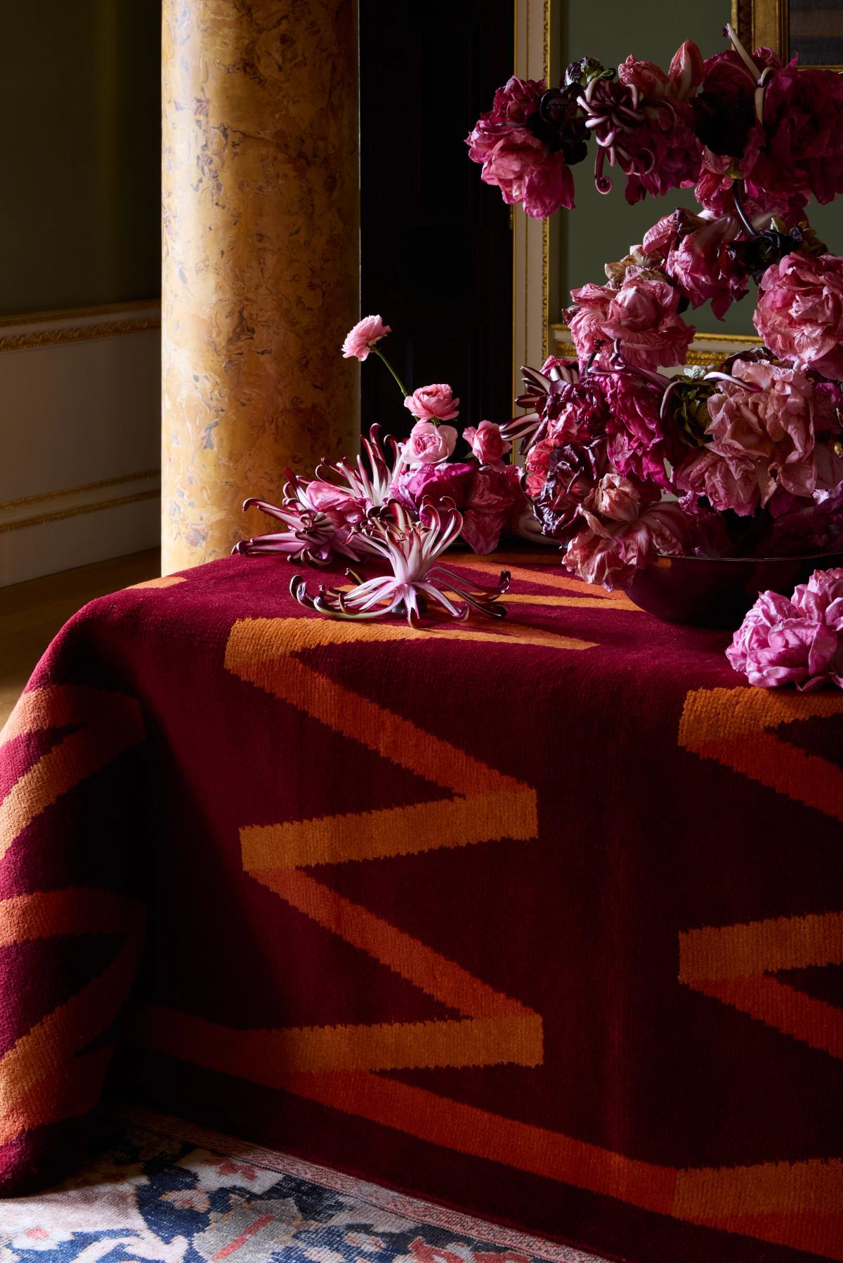 Plush wool rug Folding Ribbon in Burgundy pictured draped on a table with an elegant pink flower centrepiece.