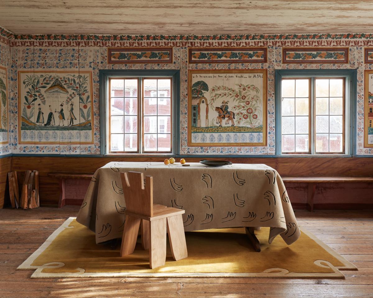 Loops – Yellow bildet eine warme Grundlage in diesem historischen Raum, wobei seine sanften Kurven den handwerklichen Charme der bemalten Wände unterstreichen. Auf dem Tisch sorgt All Hands – Beige mit seinem verspielten Handmotiv für einen modernen, grafischen Kontrast.