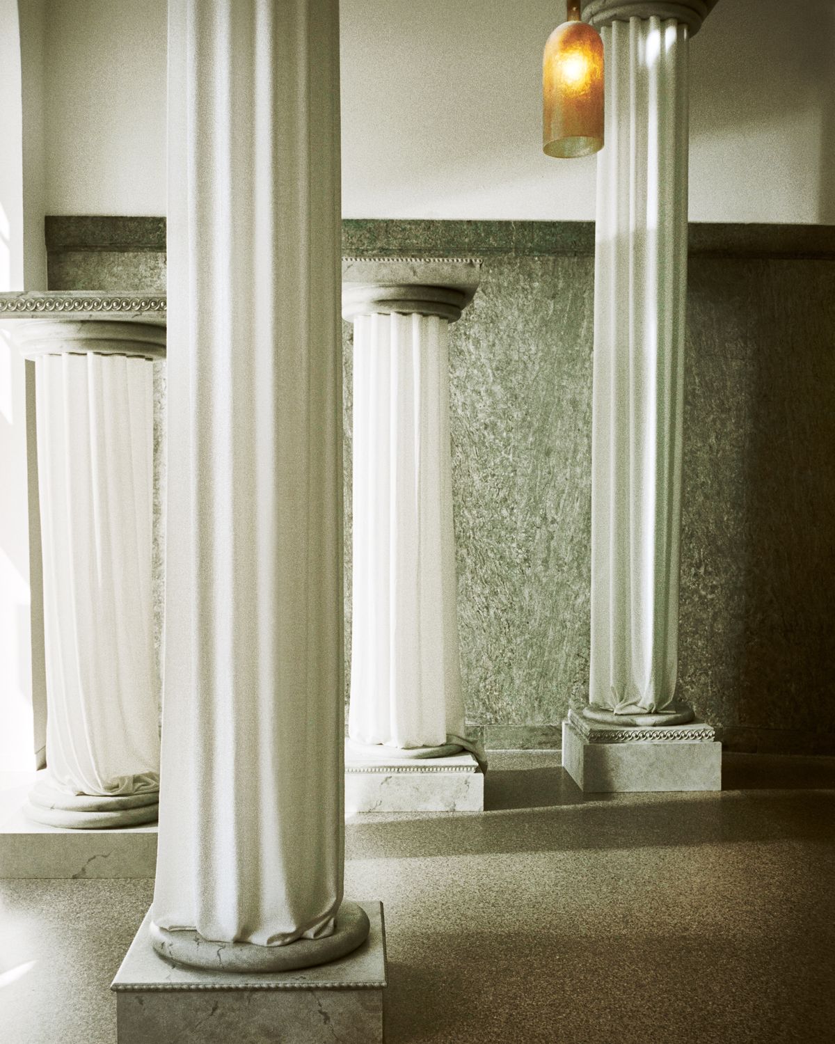 The Grand curtains on an ancient greek style pillar in the Stockholm Flagship with the light shining in through the windows onto the green marble interior.