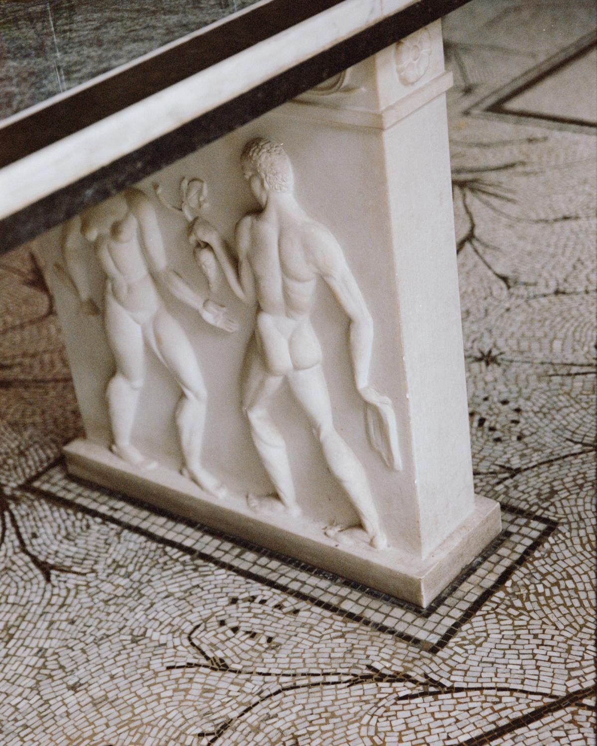 Photo d’une gravure en marbre représentant deux corps, avec un sol orné d’une fresque murale.