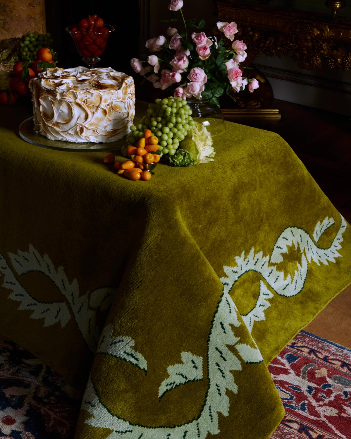 Plush wool rug Climbing Vine in Olive pictured draped over a table with a decadent cake and flowers.