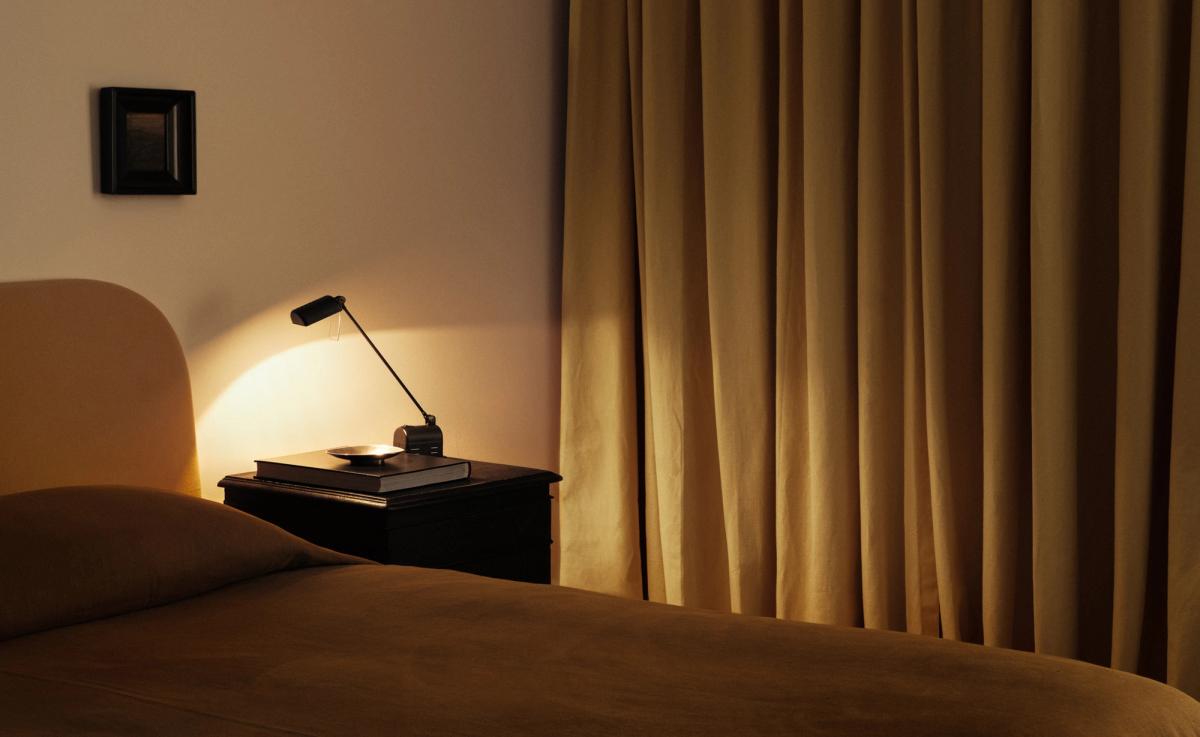 Les rideaux The Blackout en coloris Leo de Nordic Knots, mis en scène dans une chambre apaisante avec du linge de lit couleur rouille et une table de chevet noire élégante.