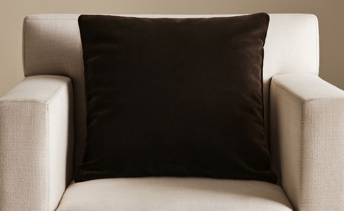 Der Teddy-Velvet-Kissenbezug in Walnut, fotografiert auf einem hell gepolsterten Sessel bei weichem, warmem Licht.