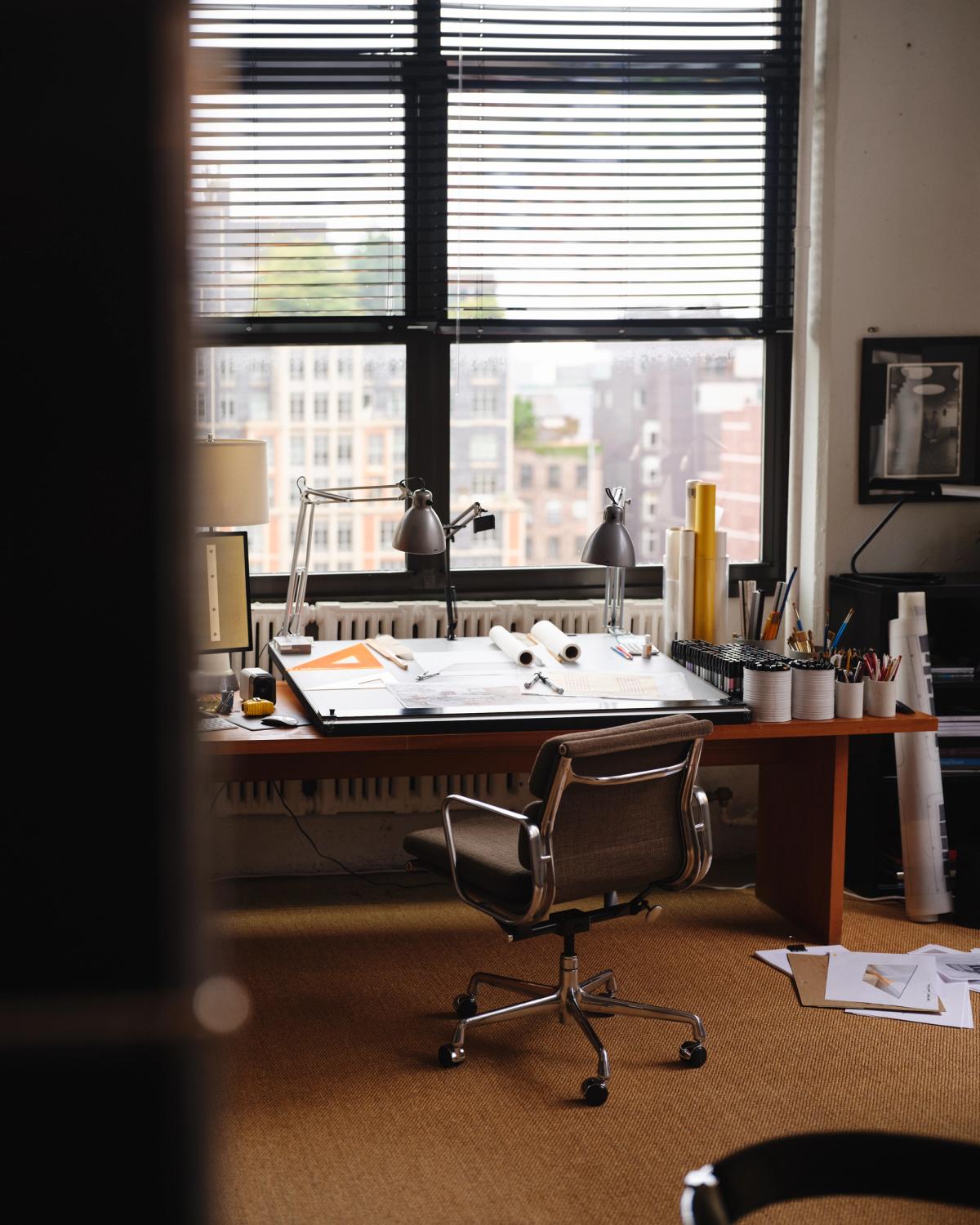 Studio Mellones arbetsstudio i New York, fotograferad med ett ritbord vid stora fönster, arkitektoniska verktyg och en stillsam, koncentrerad arbetsmiljö.