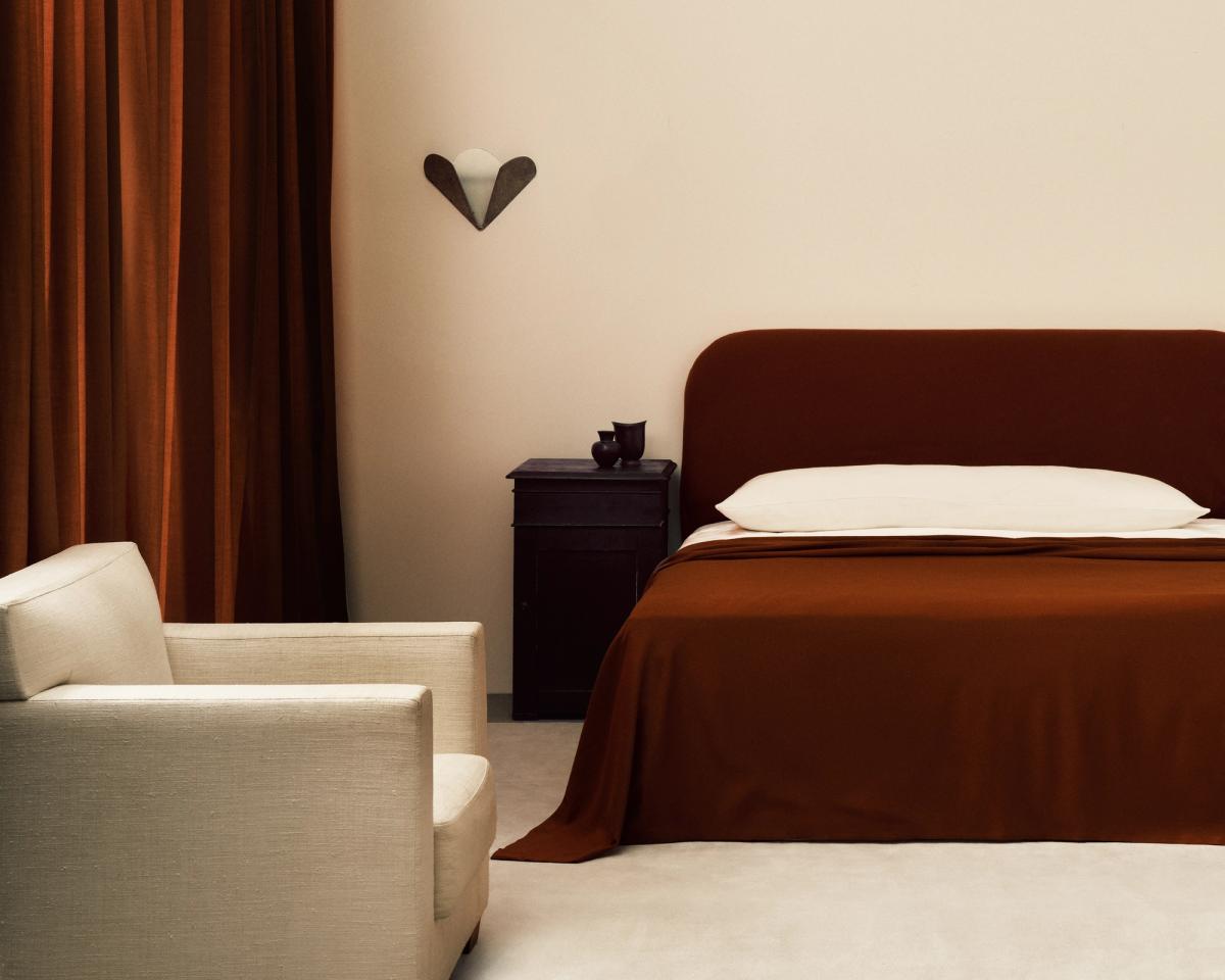 Les rideaux The Grand en Burnt Red photographiés dans une belle chambre avec des détails de décoration intérieure noirs et un lit aux draps rouges.