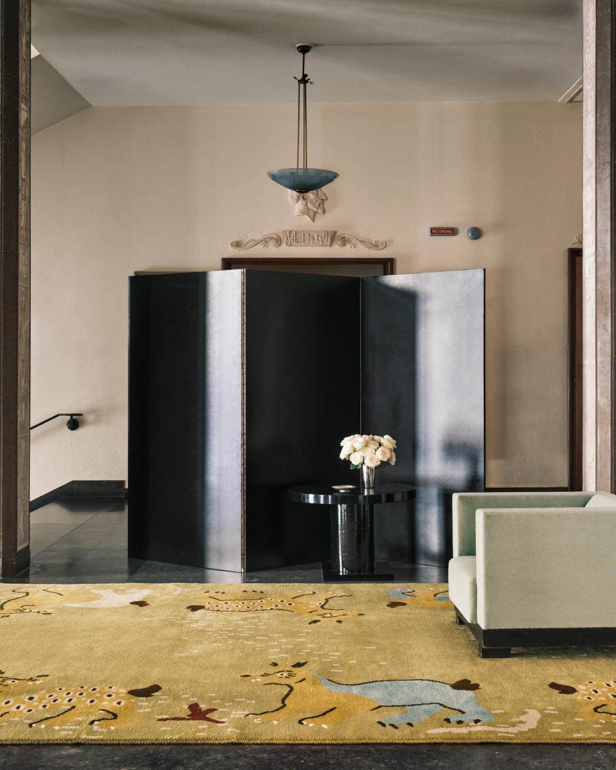 Grace 03 – Fauna — im Stockholmer Konzerthaus inszeniert. Ein gold-beiger Teppich mit verspielten Tierformen und organischen Mustern, kombiniert mit skulpturalen Möbeln und neoklassischen Elementen.