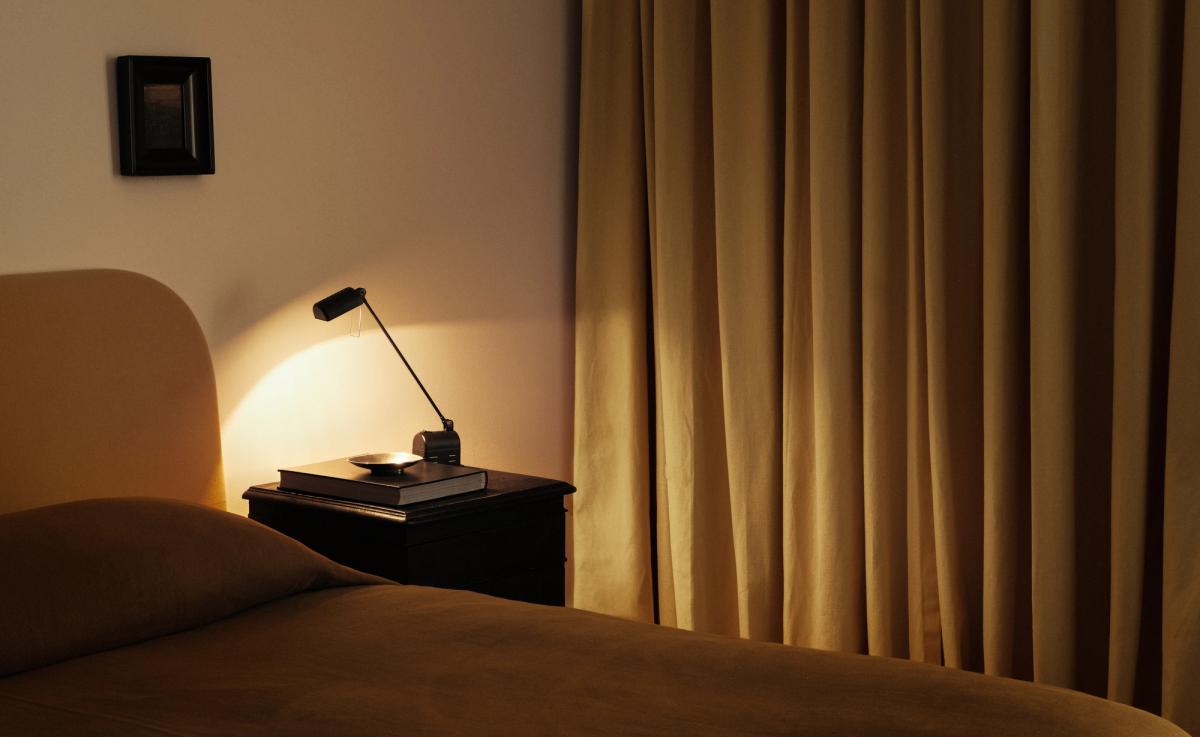 The Blackout curtains in Leo are shown in a softly lit bedroom with matching warm tones, featuring a neatly made bed, dark nightstand, and reading lamp.