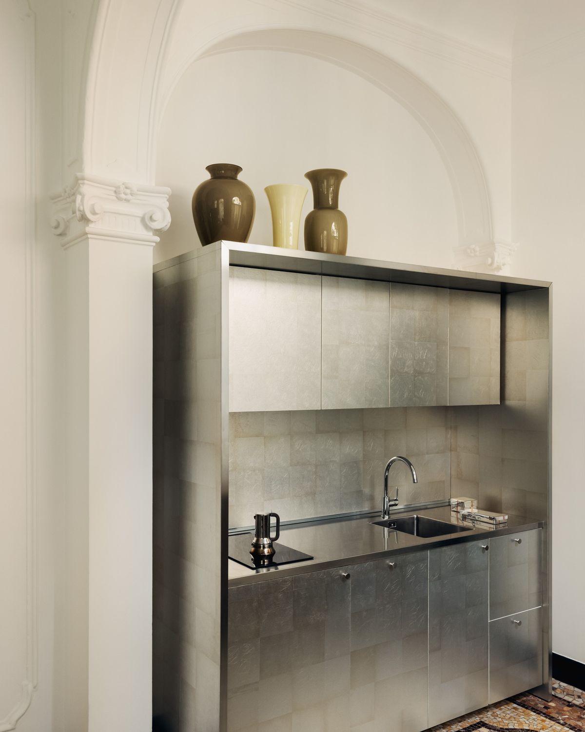 Eine reduzierte Küche in einem historischen Mailänder Interieur mit Edelstahlmöbeln, gewölbten Decken und kuratierten Keramikgefäßen.