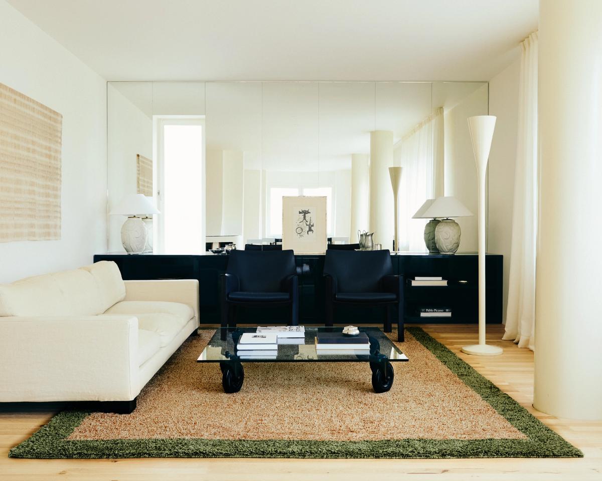 Tapis en laine shaggy Ryya en Beige, photographié dans un salon lumineux avec des détails d’intérieur noirs et un canapé blanc.