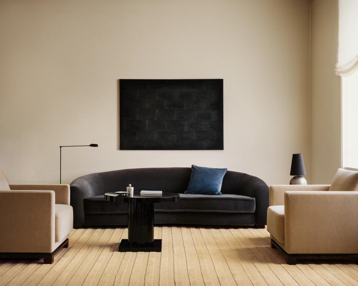 Tapis Park 03 en Sunrise – un tapis aux tons dorés chaleureux avec des rayures verticales ton sur ton, ancrant un salon minimaliste avec un canapé foncé et un mobilier sculptural.