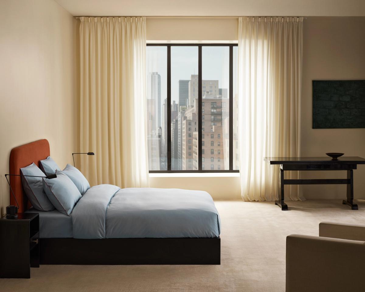 Signature Headboard in Burnt Red mit dem Percale Bettbezug in Shirt Blue/Red, fotografiert in einem hellen Schlafzimmer mit transparenten Vorhängen und großem Fenster.