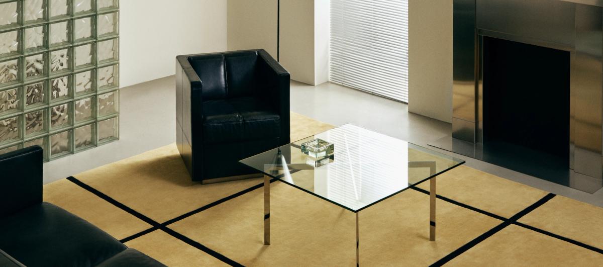 Minimalistisk interiör med svarta lädersittplatser, ett soffbord i glas och mattan Pavilion – Yellow.