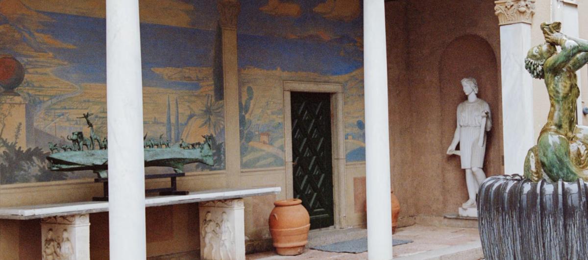 Innergård med väggmålning, statyer och klassiska kolonner.