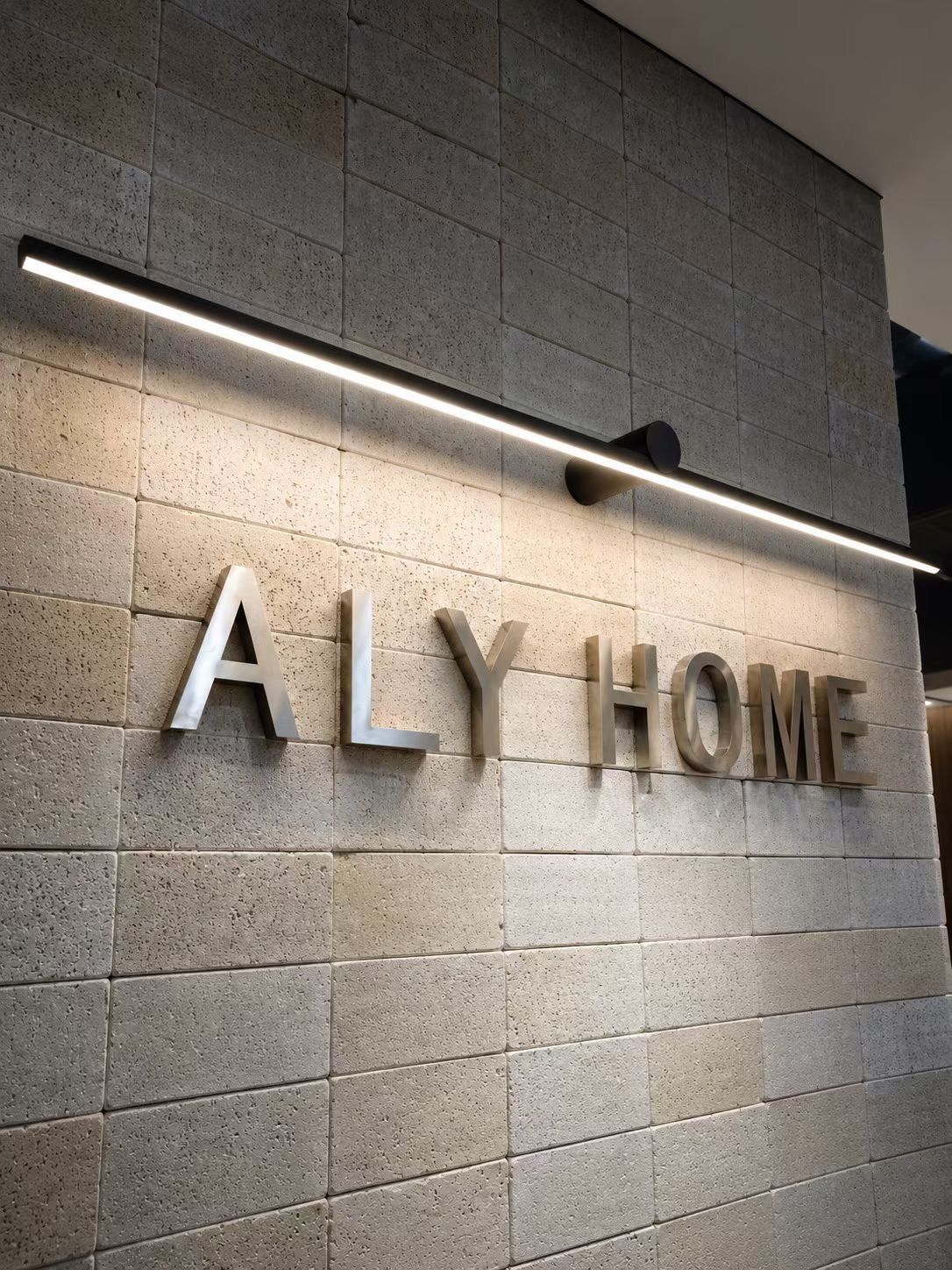 ALY HOME reception wall with metal letters on a textured concrete block surface at R+T Asia 2025