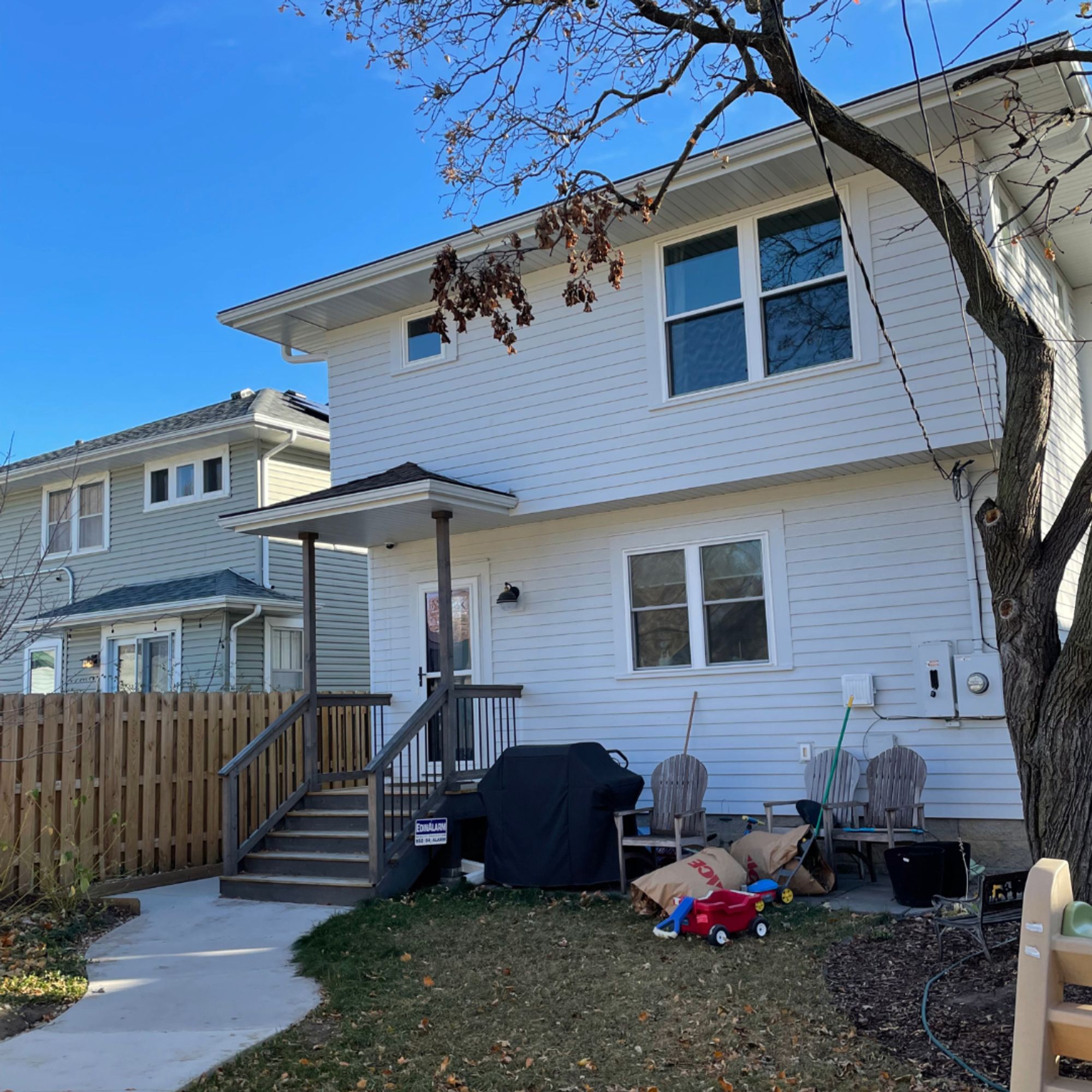 Rear of a two-story white house with a small covered porch, wood steps and backyard fence - Mom's Design Build
