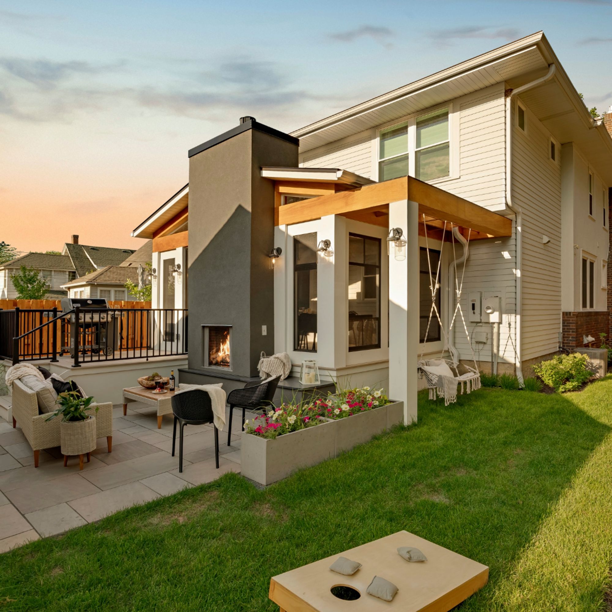 Backyard patio with stucco fireplace, seating, planter boxes, and covered porch with hanging swing at dusk - Mom's Design Build