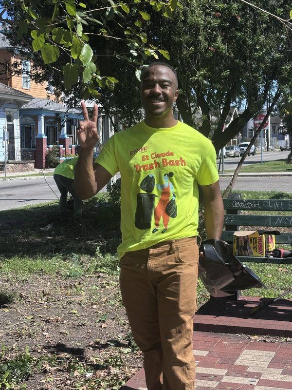 A smiling volunteer in a Trash Bash shirt throwing up a peace sign