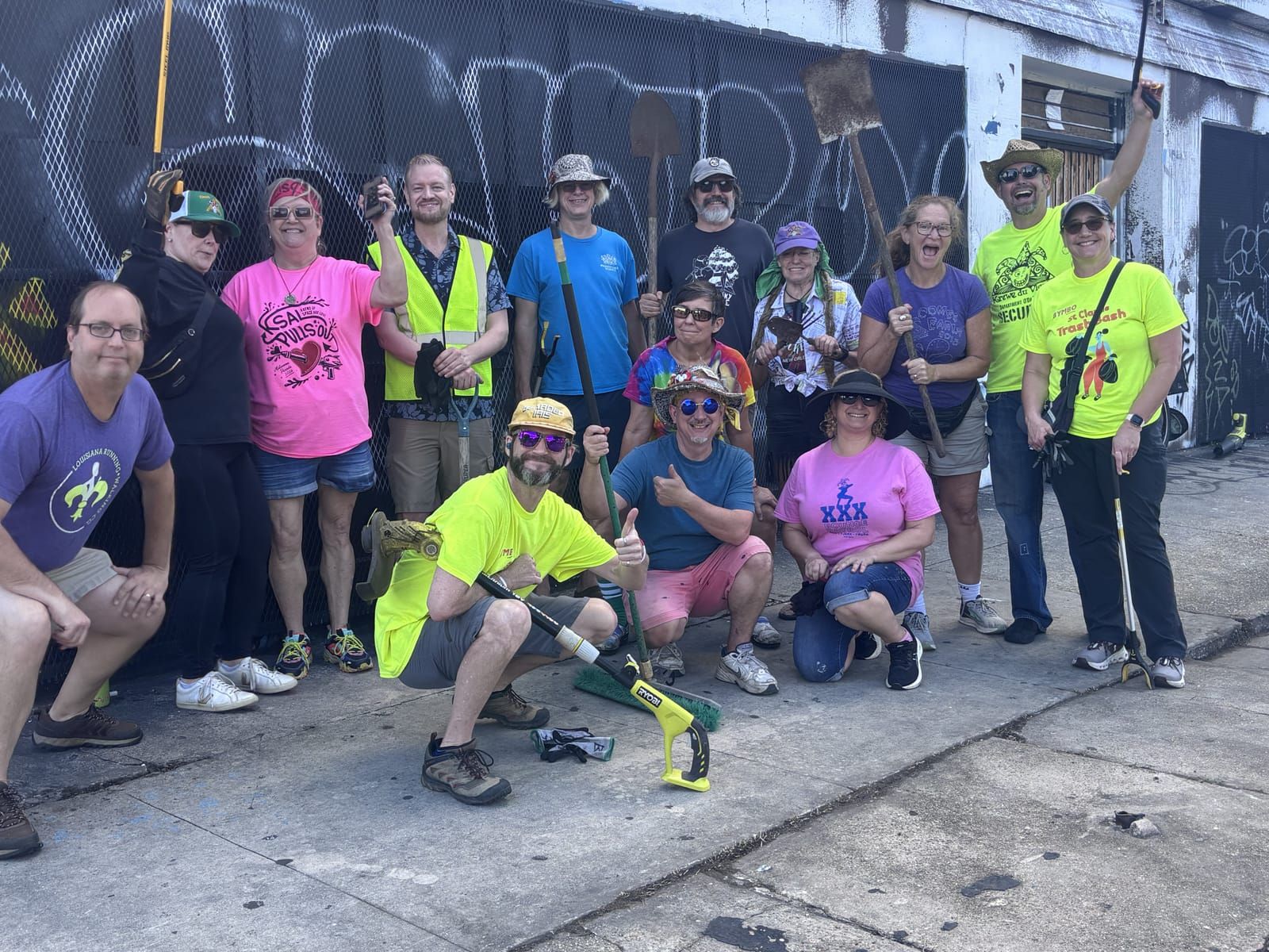 A big group of Trash Bash volunteers with grabbers and brooms posing together on St. Claude