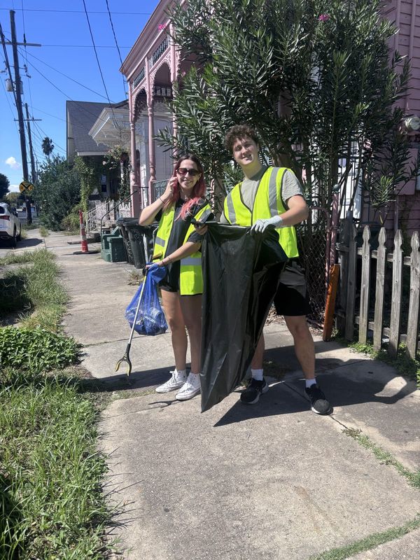 Two volunteers in safety vests holding open a trash bag on the sidewalk