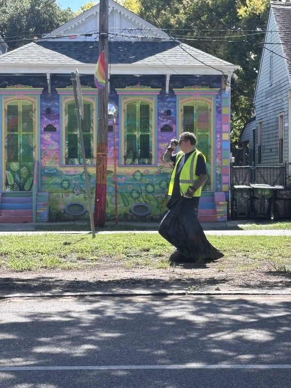 A volunteer in a safety vest cleaning up in front of a brightly painted house