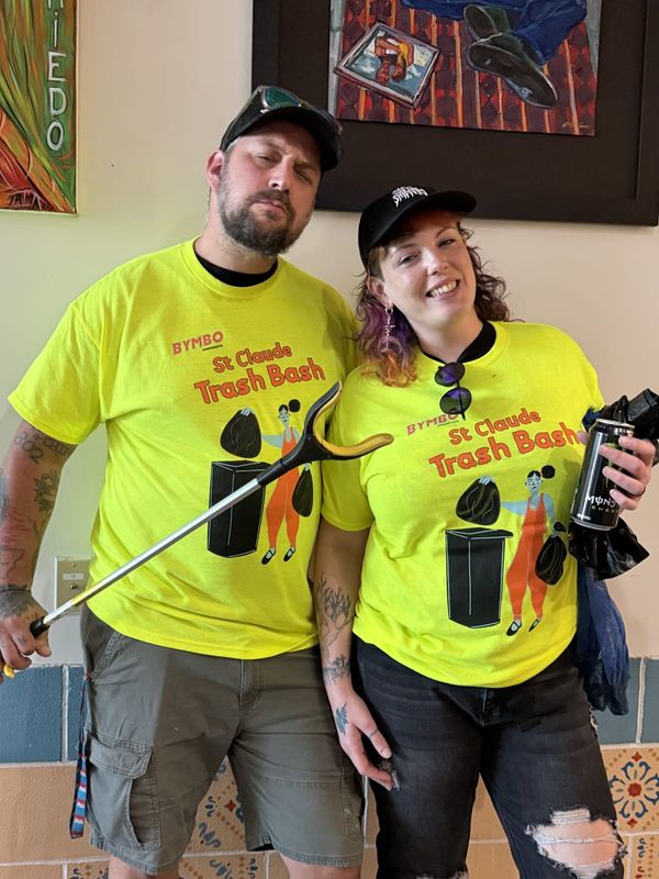 Two volunteers in neon St. Claude Trash Bash t-shirts holding a trash grabber