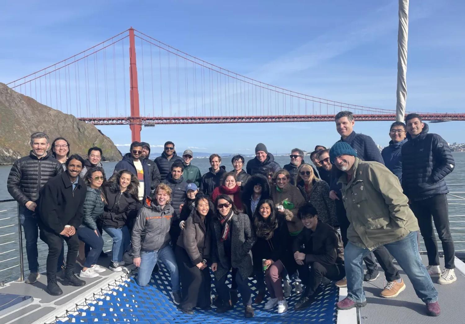 Group of people posing for a photo on a boat with the Golden Gate Bridge and blue sky in the background.