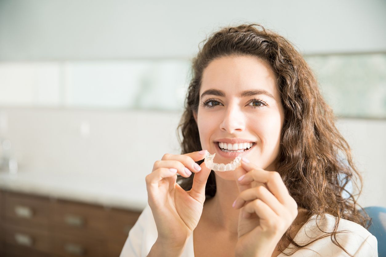 Beautiful young woman holds Invisalign clear aligner in front of smile