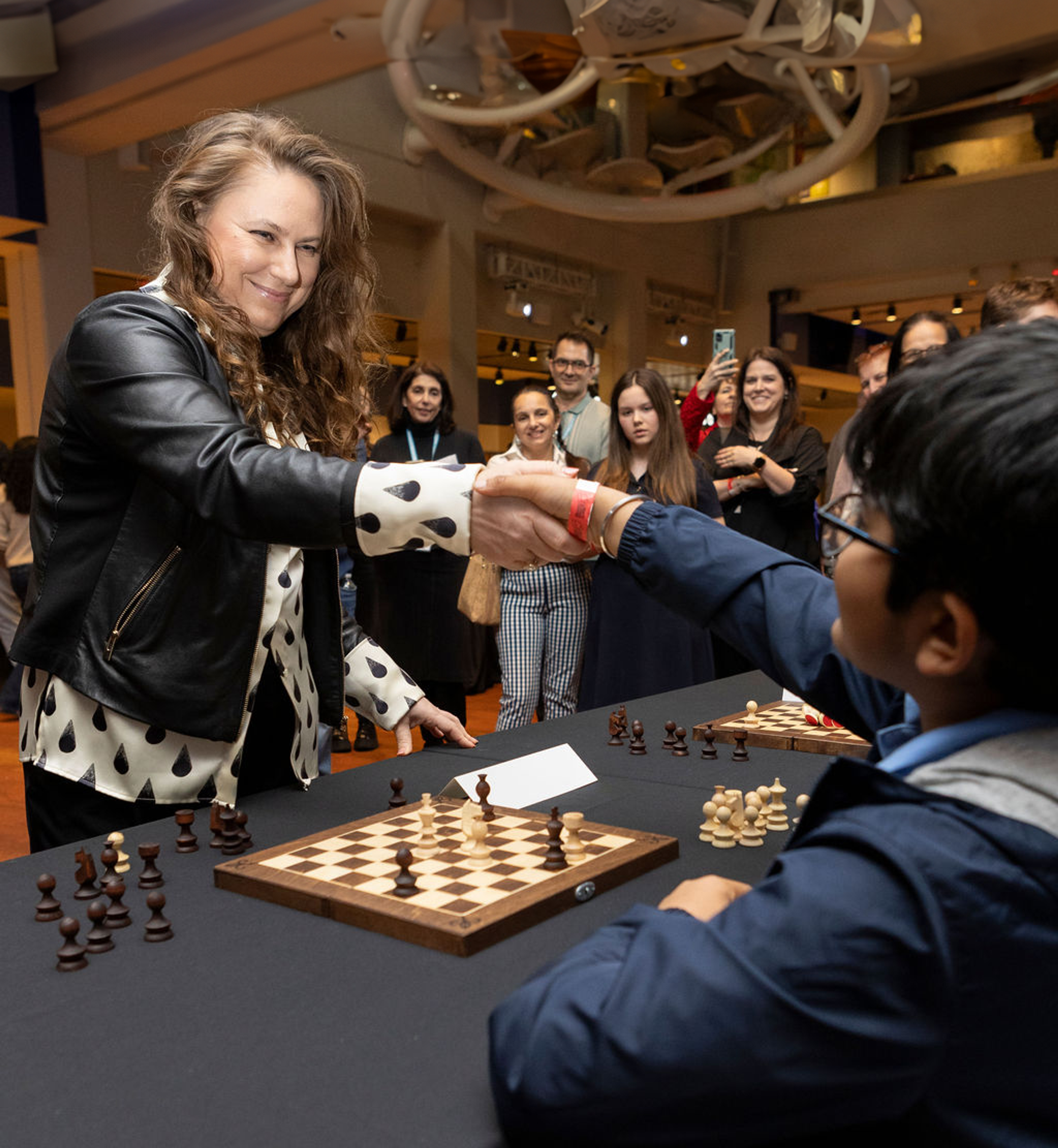 woman and student shaking hands over a game of chess