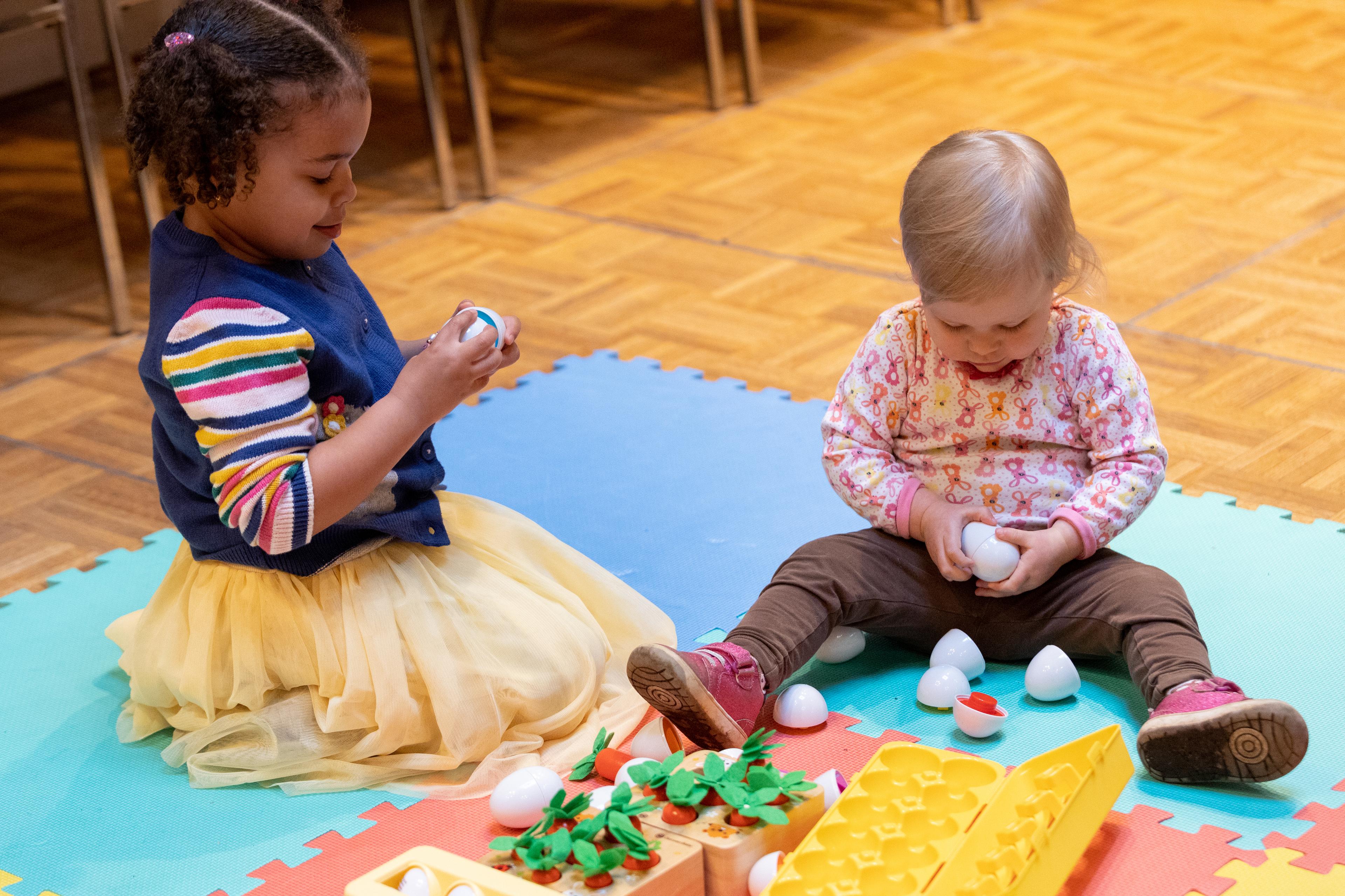 two young girls sitting on the floor holding easter eggs