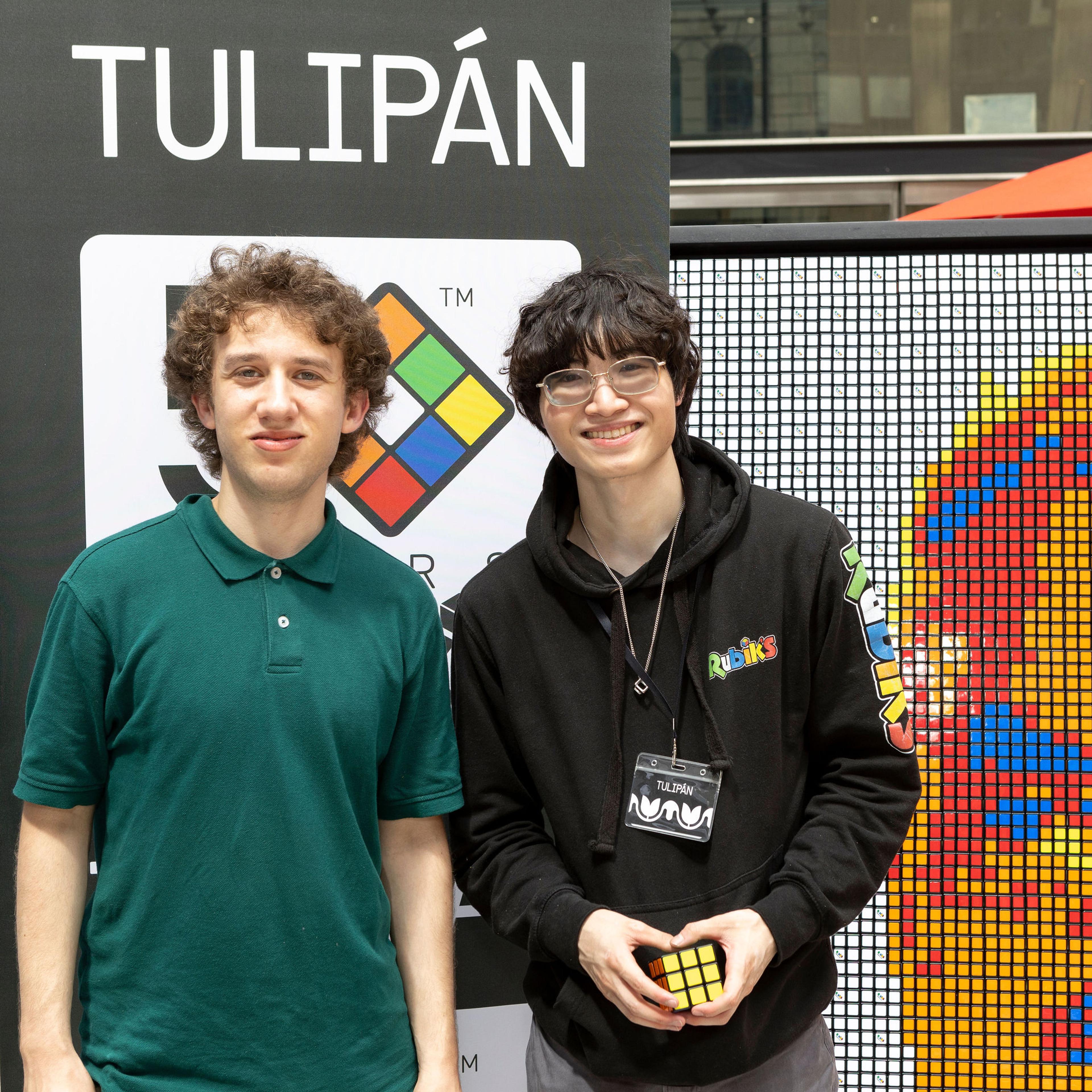 two young men holding a rubiks cube in front of a banner