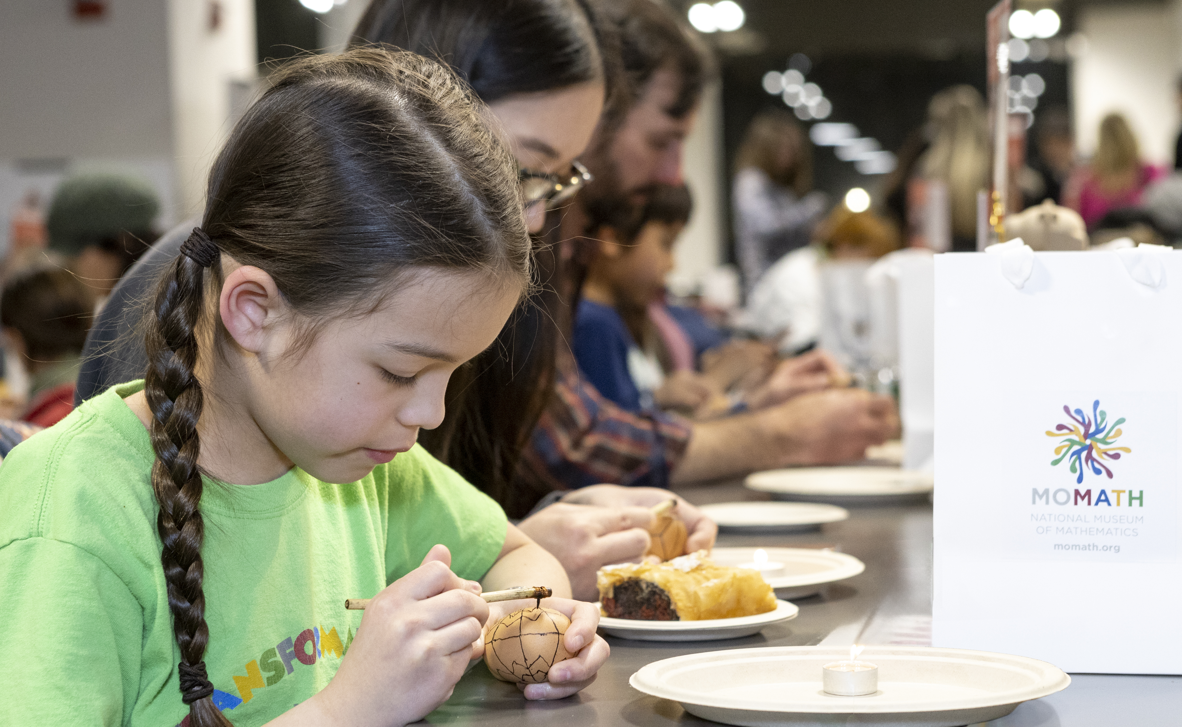 young girl painting an egg at a table with others blurred in background