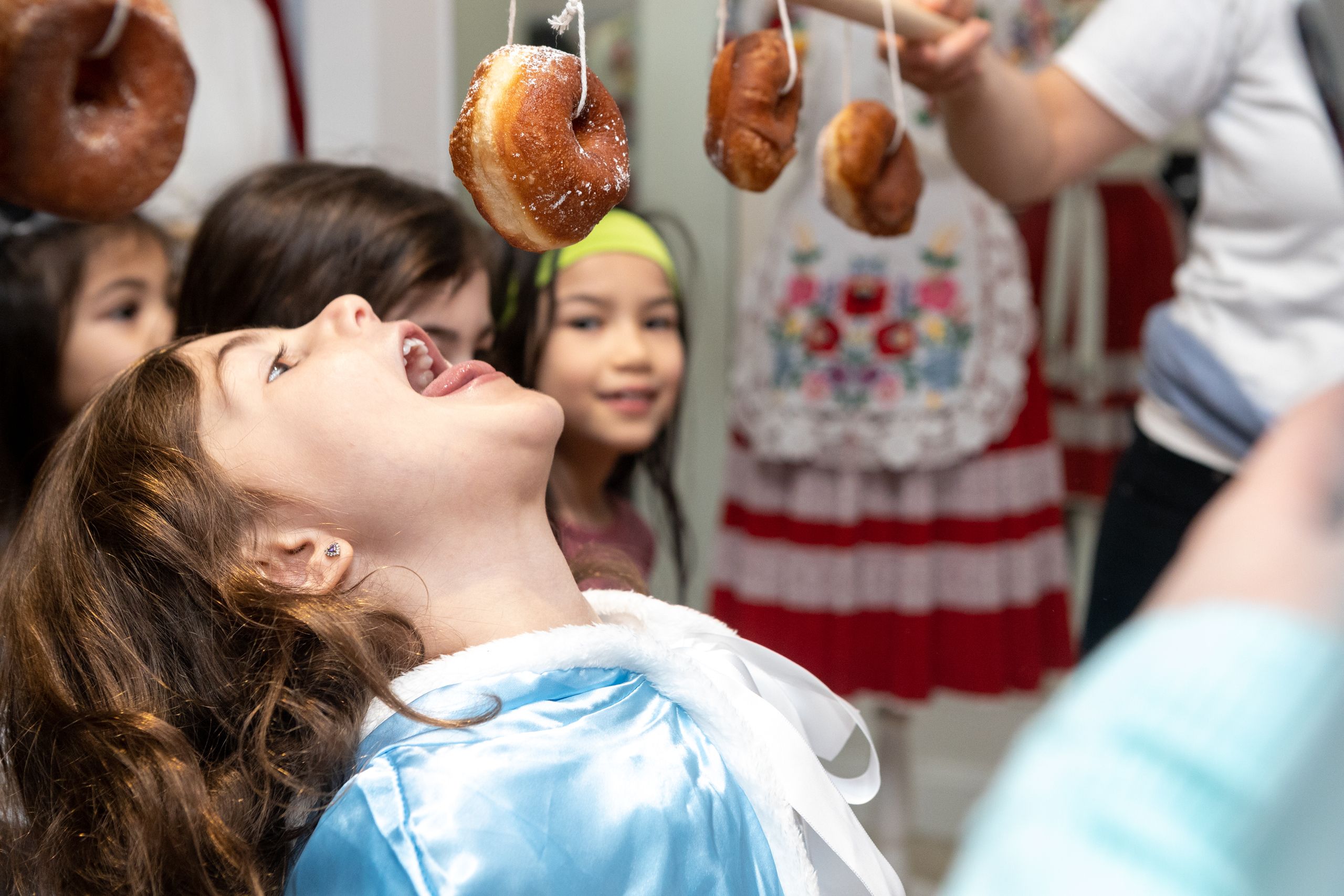 a young girl eating a donut hanging from a string