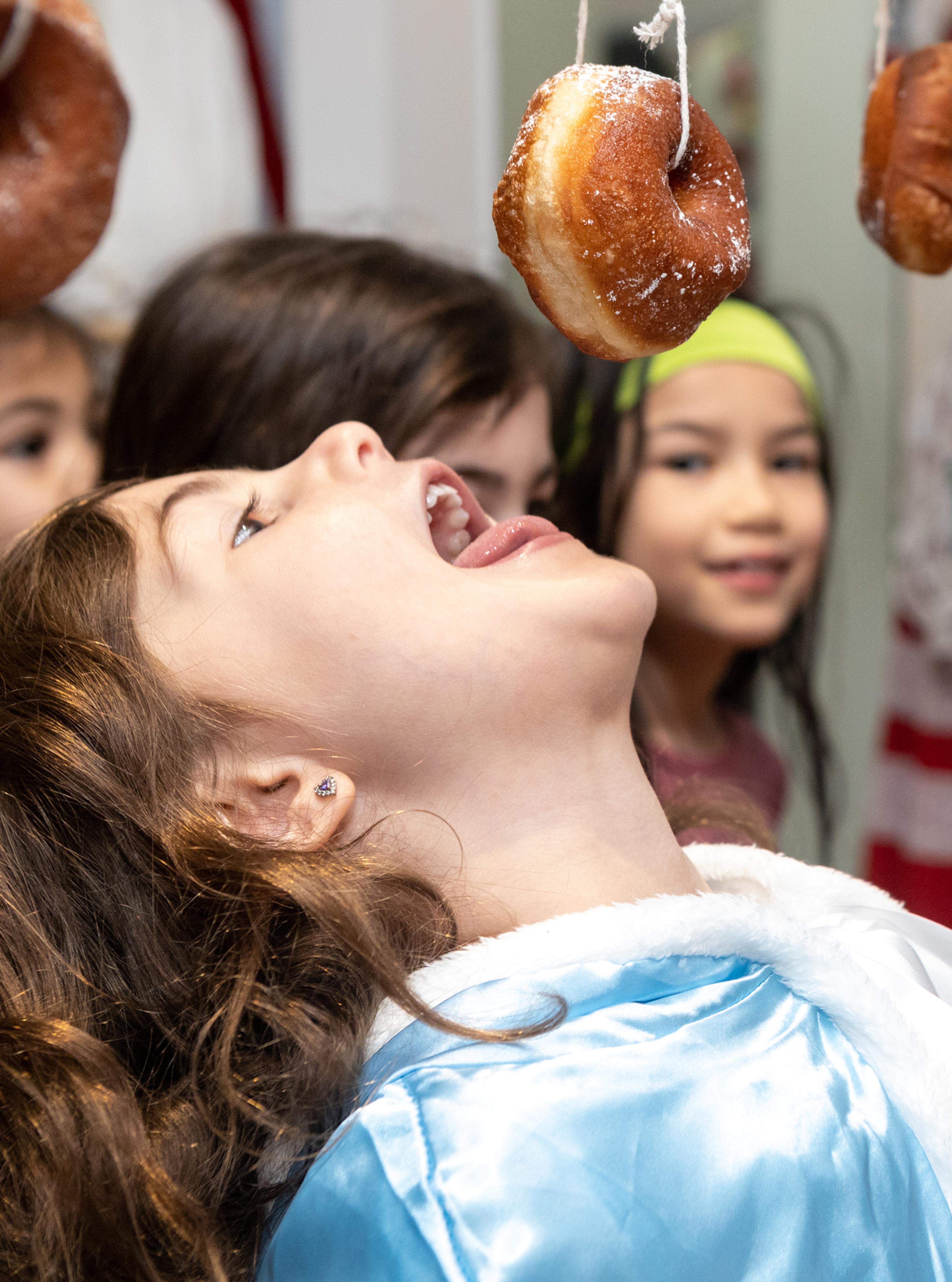 a young girl eating a donut hanging from a string