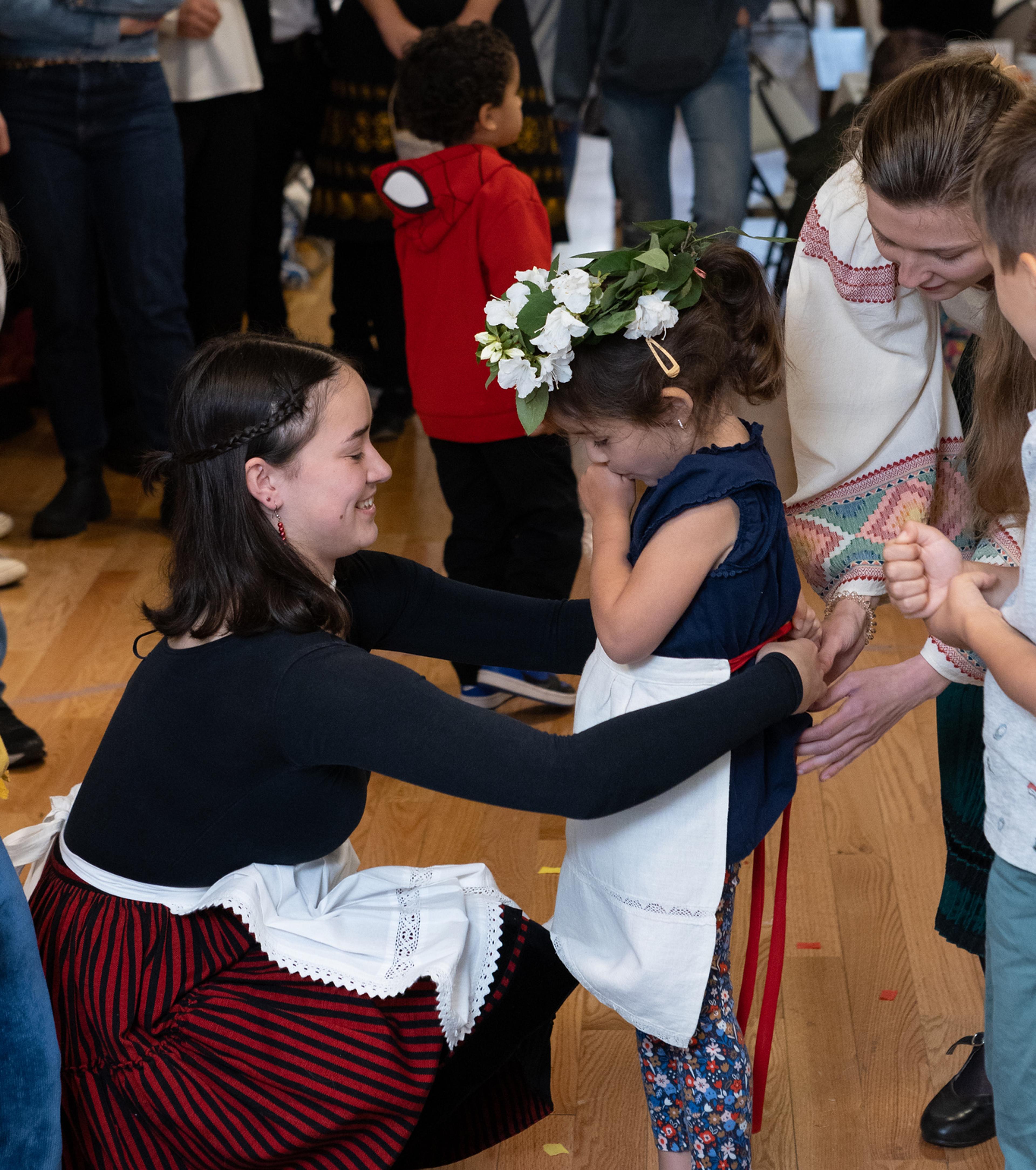 woman wrapping an apron on a little girl with flowers on her head