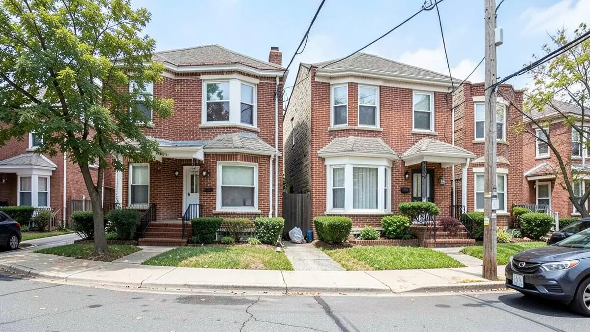 Attached brick two-family homes with small front yards on a residential street in Corona, Queens, NY