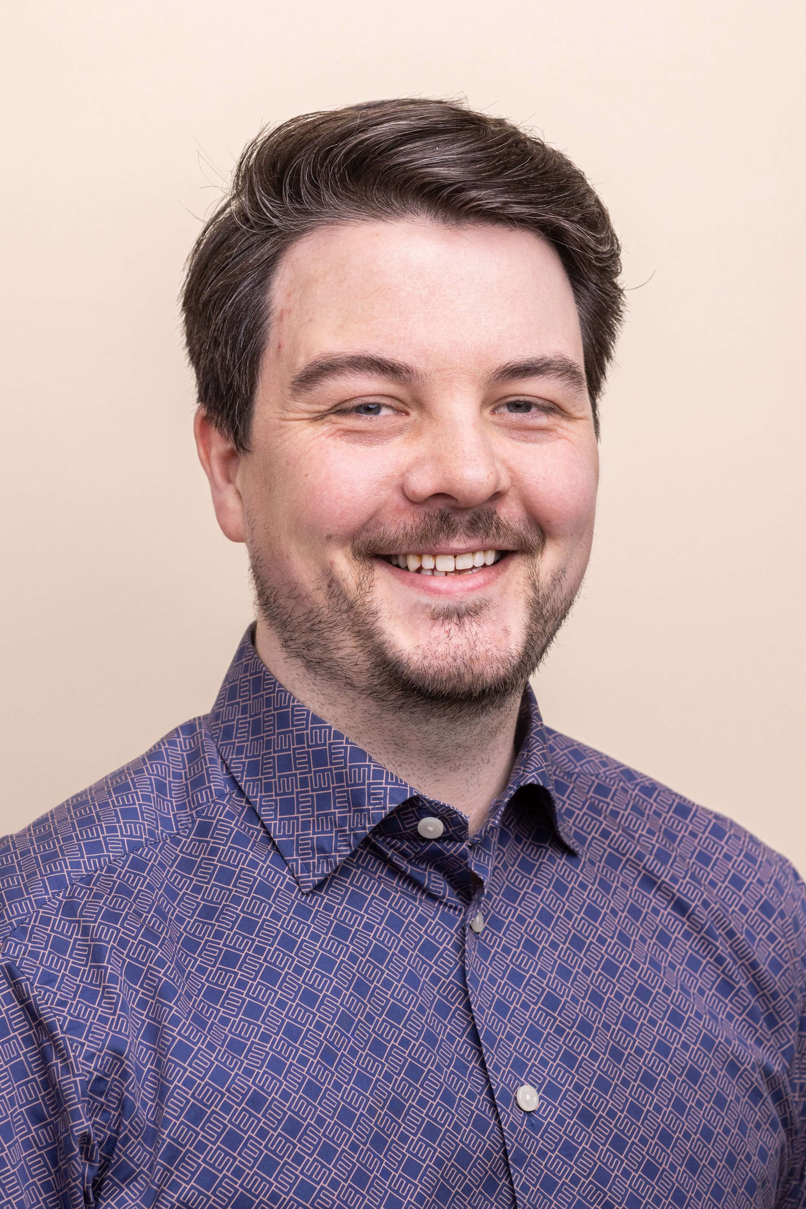 a man with a beard and a blue shirt is smiling for the camera .