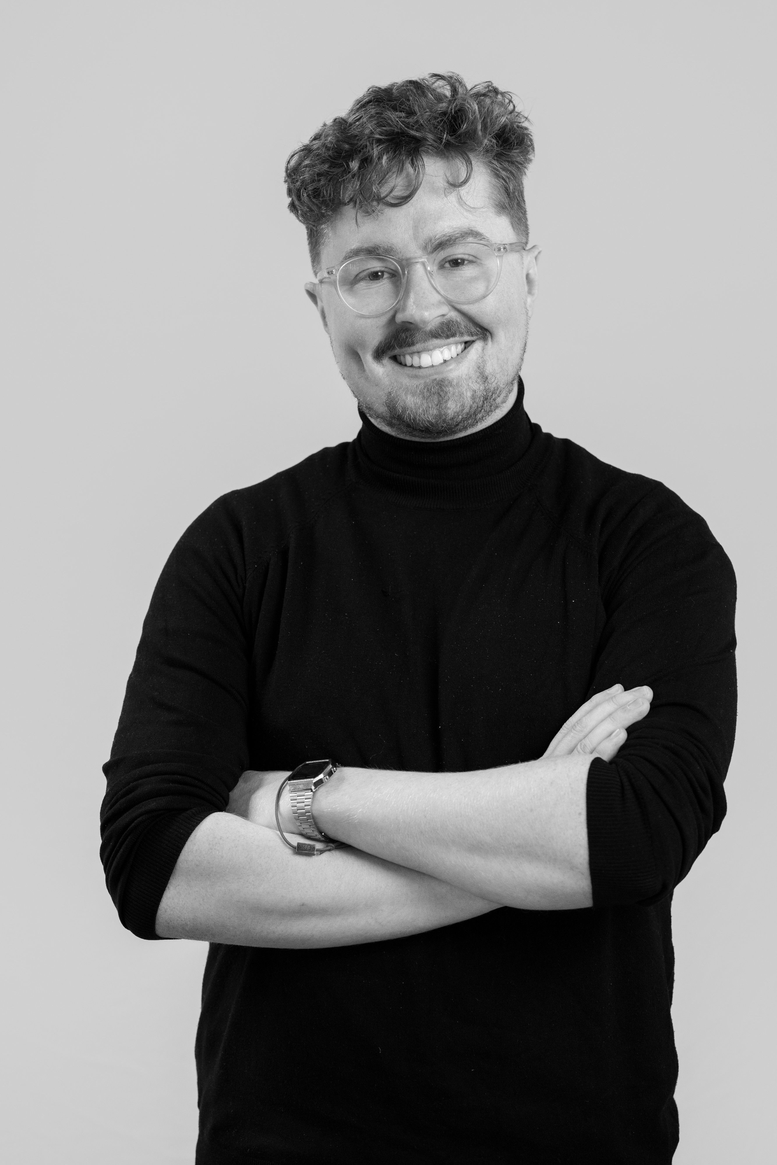 portrait of a a man with glasses folding his arms, smiling.