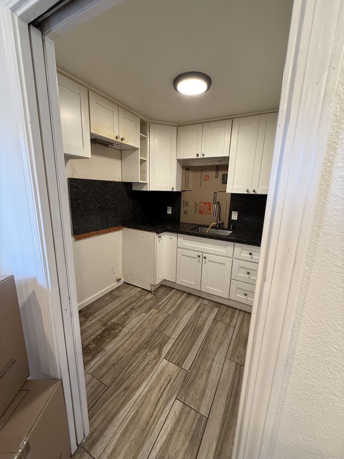 Small kitchen inside an unpermitted accessory dwelling unit with white cabinets, dark countertop, and wood-look tile floor