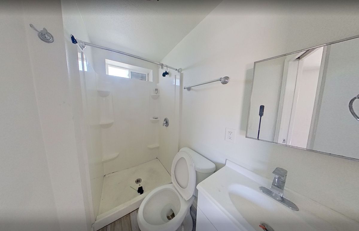 Bathroom inside an unpermitted garage conversion with a shower stall, toilet, vanity, and small window