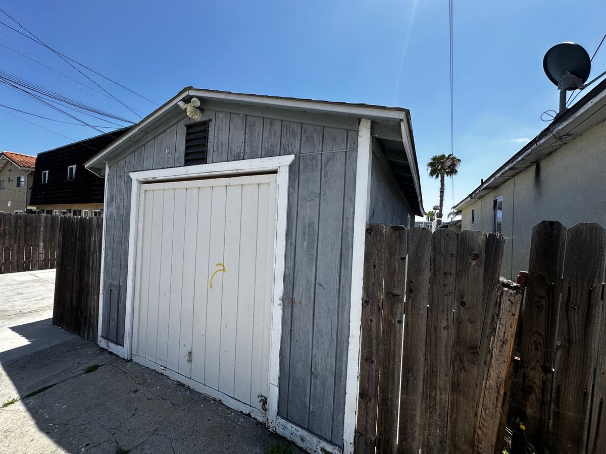 Exterior of a detached garage that was converted into living space without permits, with a wood fence and driveway