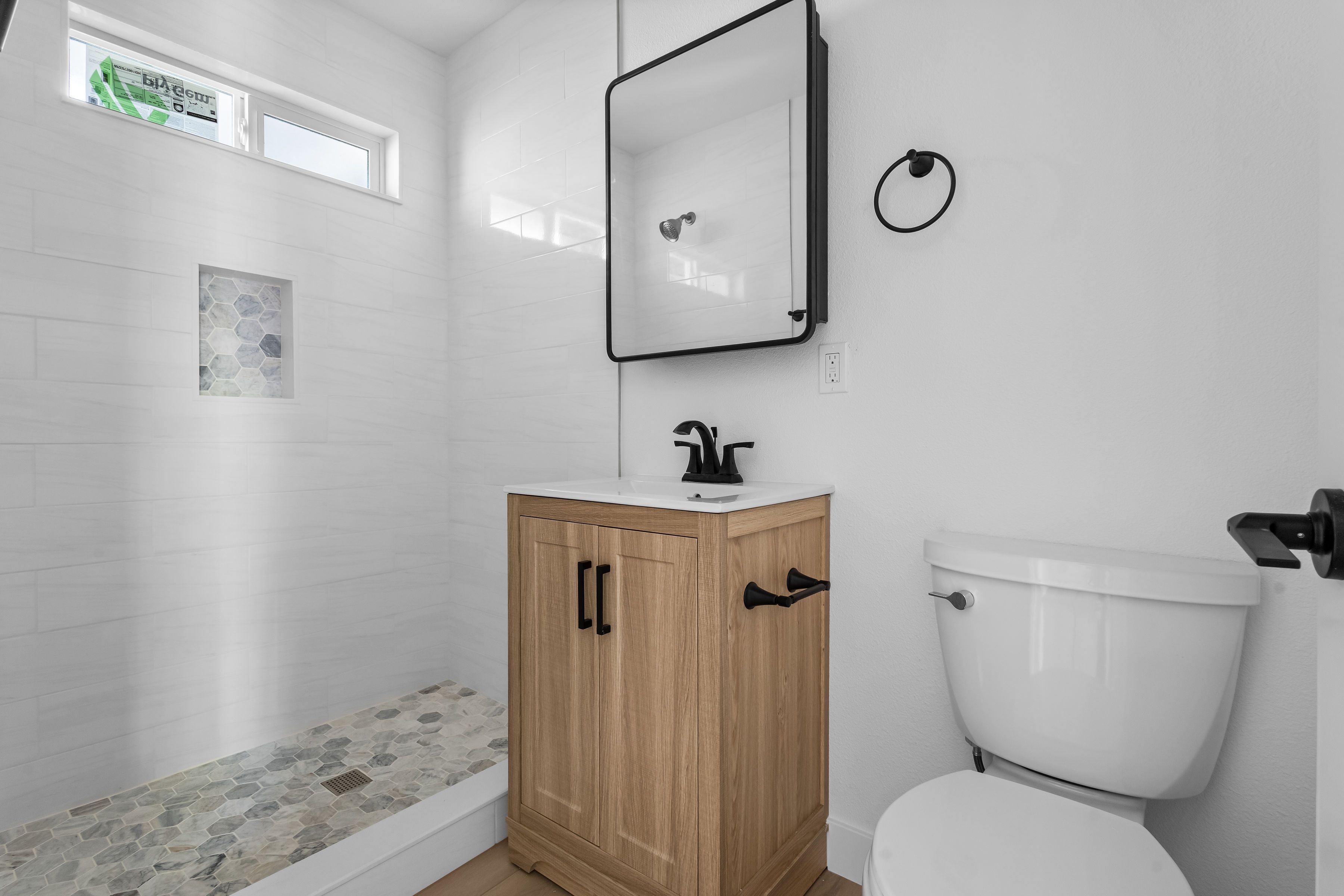 A modern bathroom remodel in San Diego featuring a custom walk-in shower with hexagonal mosaic floor tiles, a light wood vanity, and matte black fixtures.