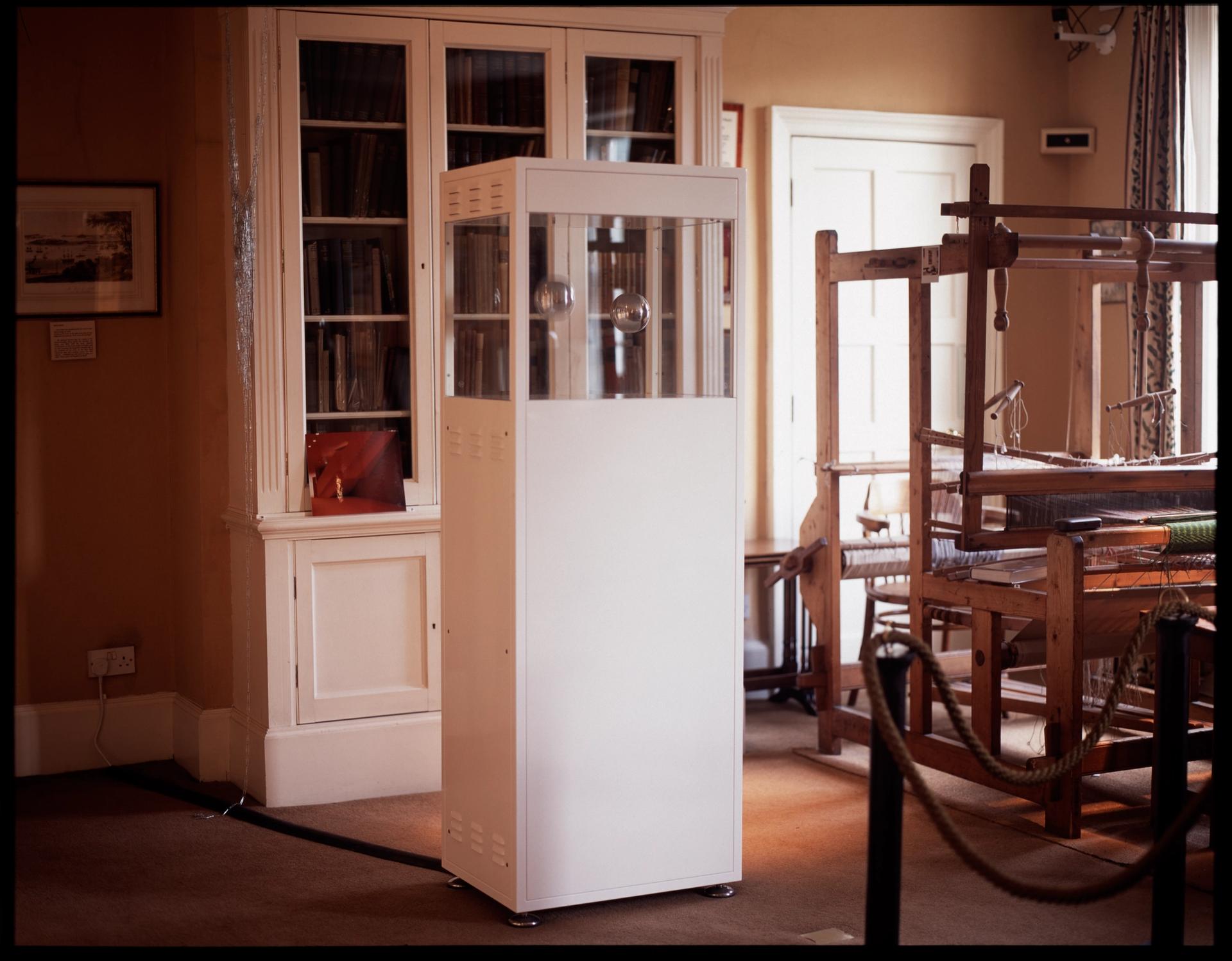 Sculpture comprising white steel cabinet next to large loom in a room with a large book cabinet