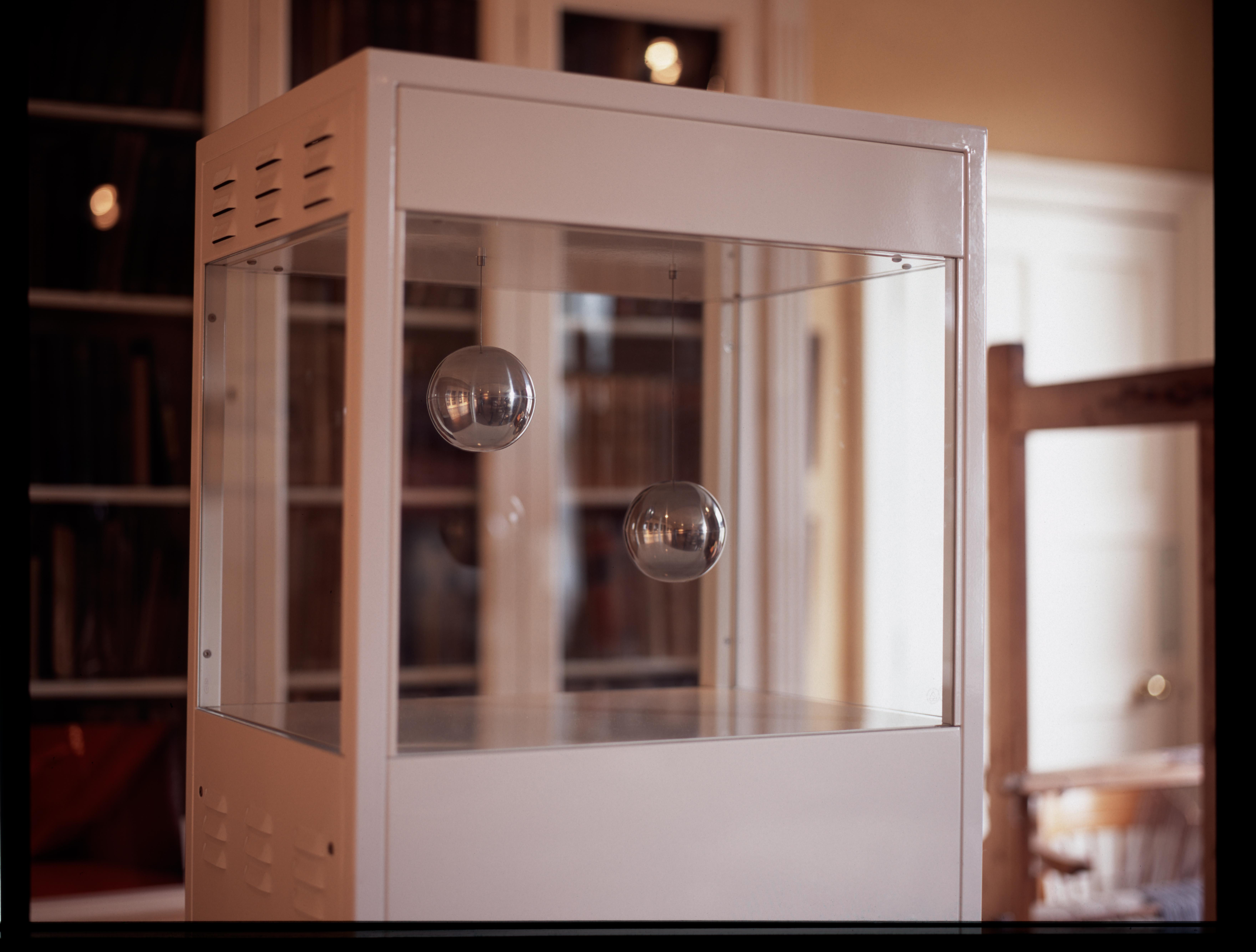 Sculpture comprising white steel cabinet next to large loom in a room with a large book cabinet