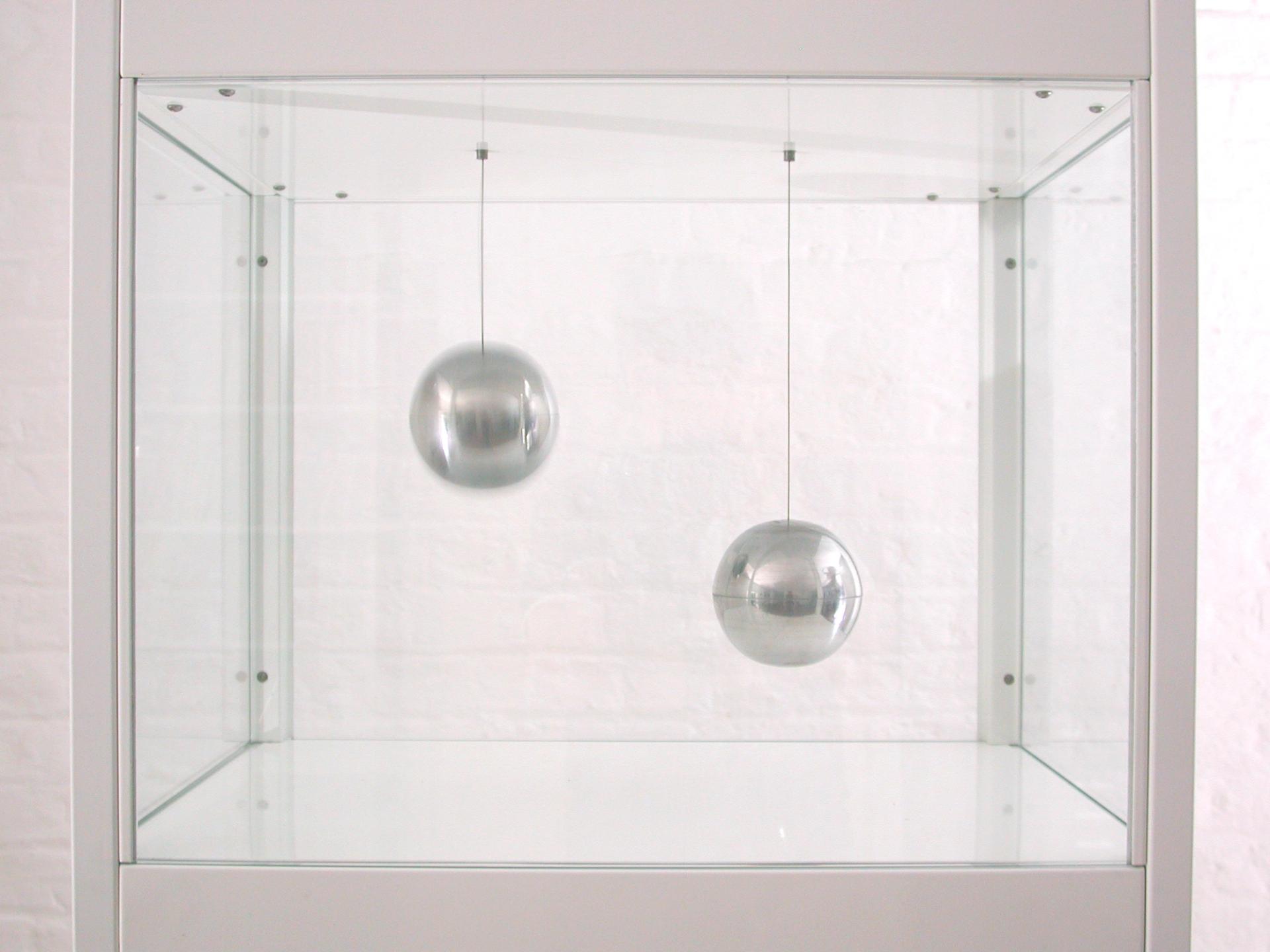 Large glass vitrine with white steel frame and two suspended shiny aluminium spheres