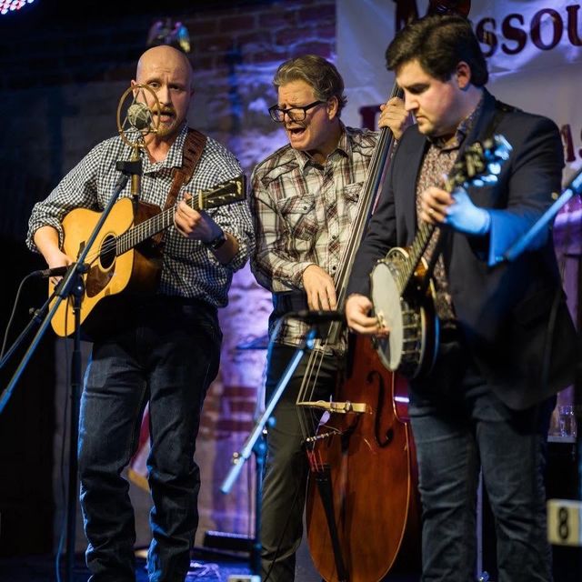 Graham Curry performing on stage with bandmates on mandolin and upright bass.