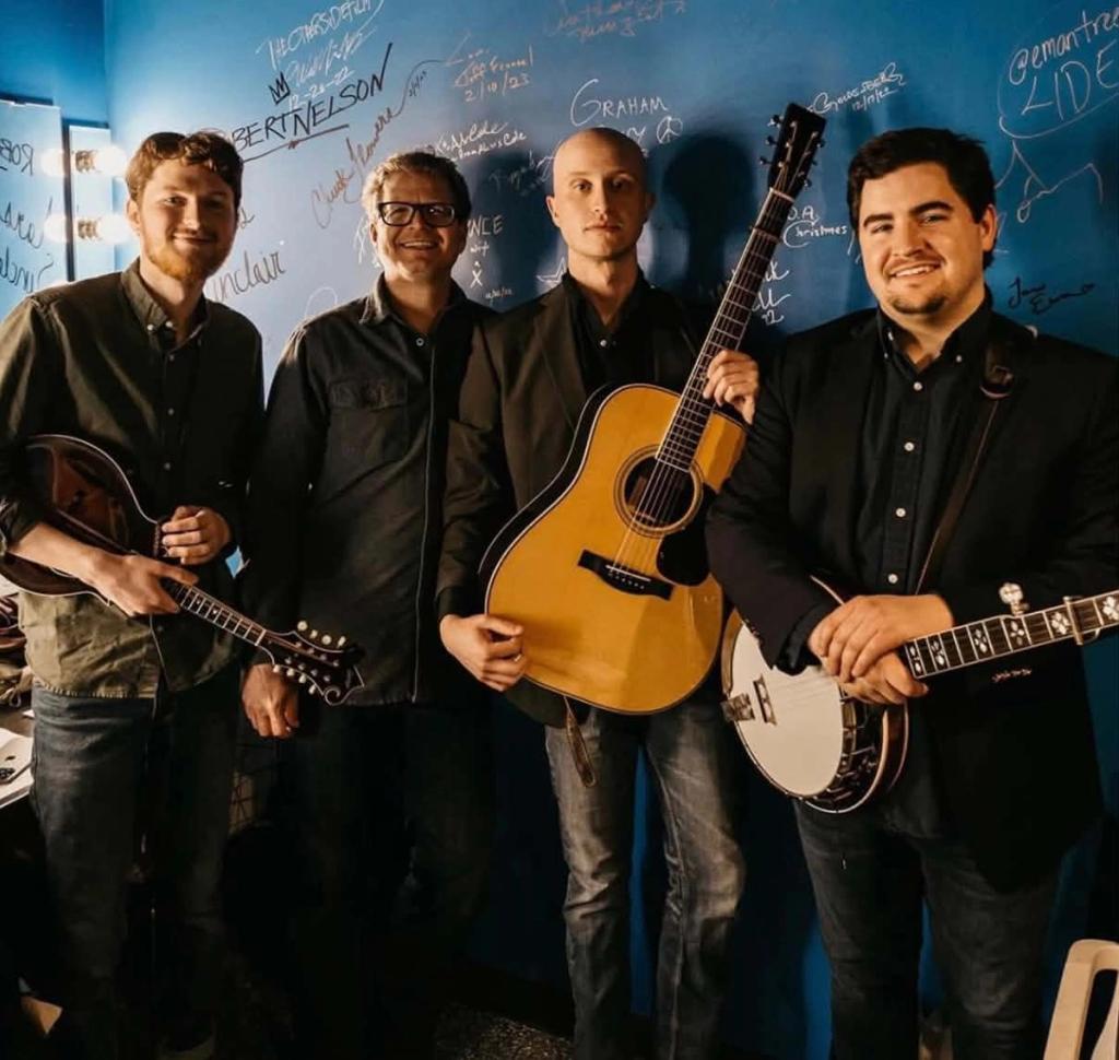 Graham Curry and The Missouri Fury standing together with their guitars and banjo in front of a graffiti-covered wall.