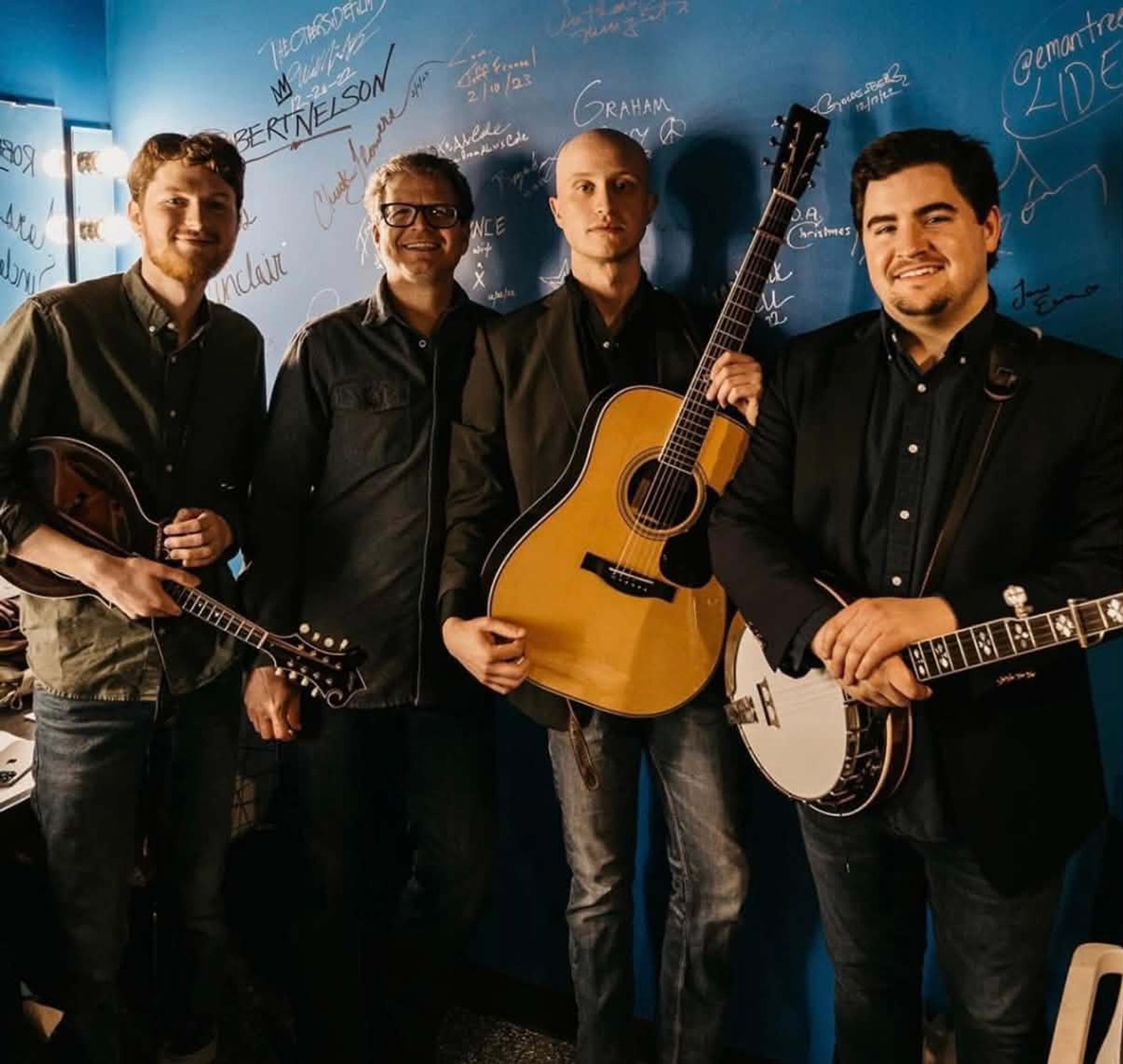 Graham Curry and The Missouri Fury standing together with their guitars and banjo in front of a graffiti-covered wall.