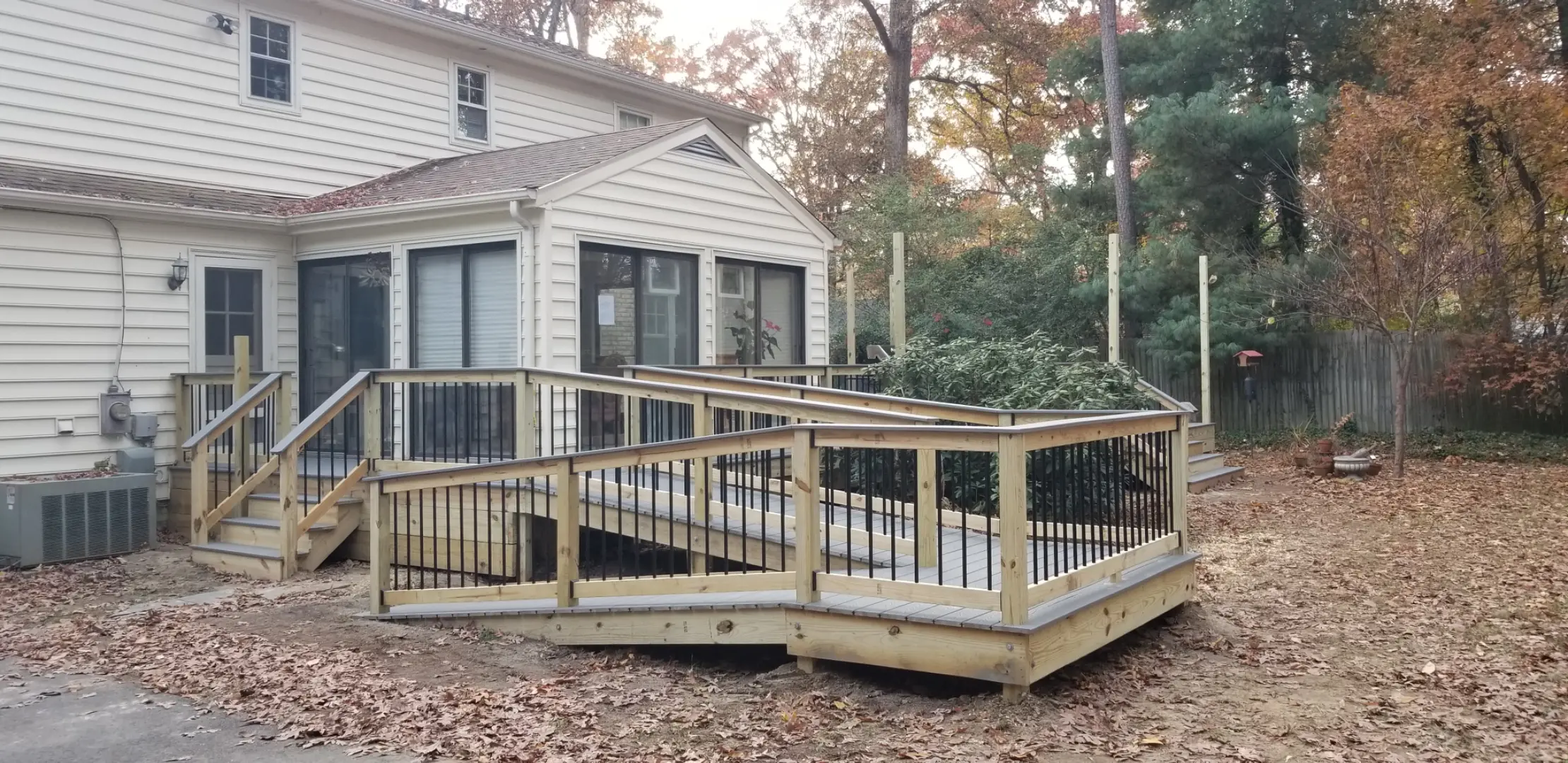 Wooden deck with a ramp and railing with black balusters attached to a house