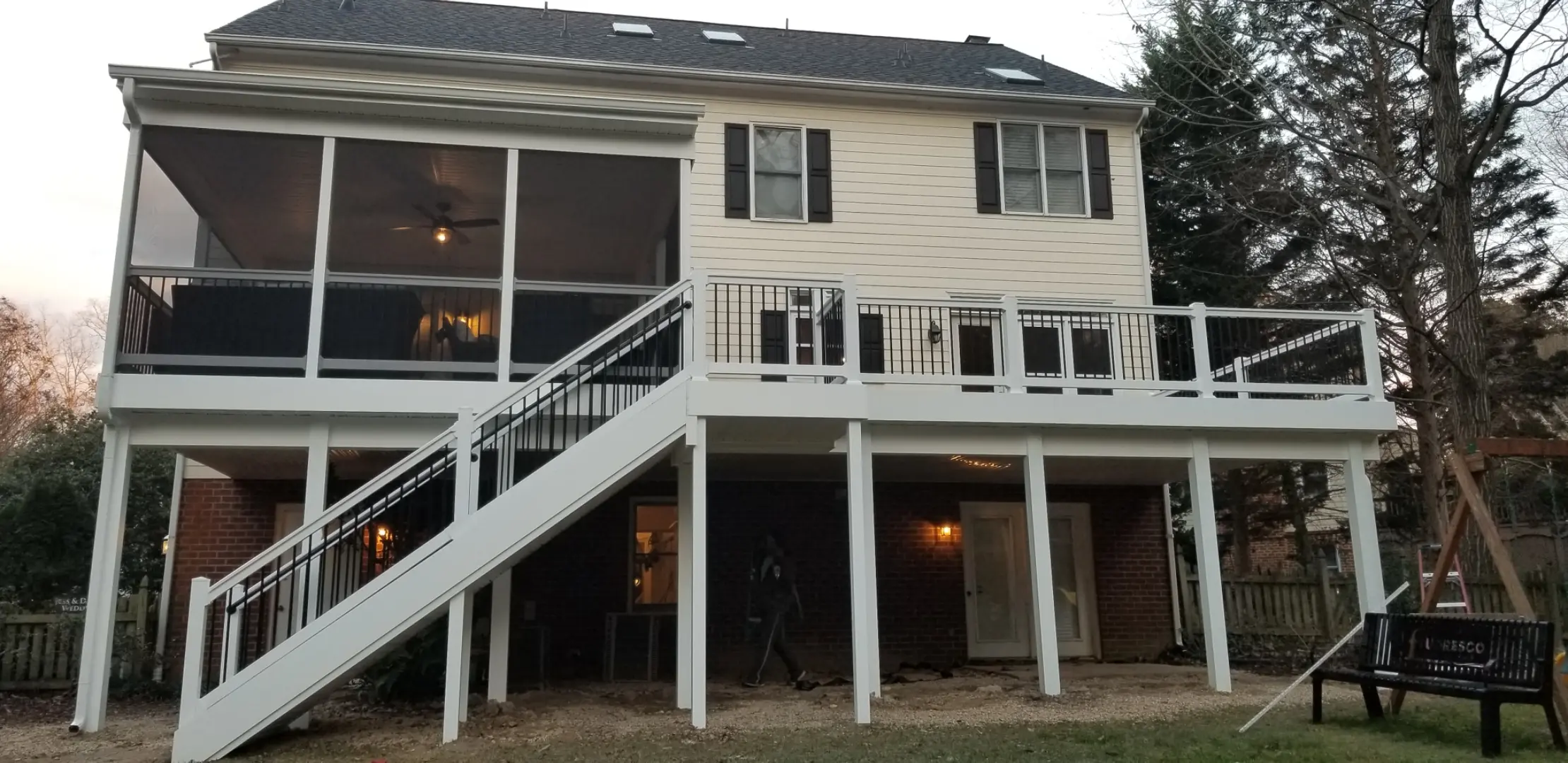 Two-story house with a screened upper deck and open lower deck, featuring a staircase on the left. The decking is made of Trex Toasted Sand
